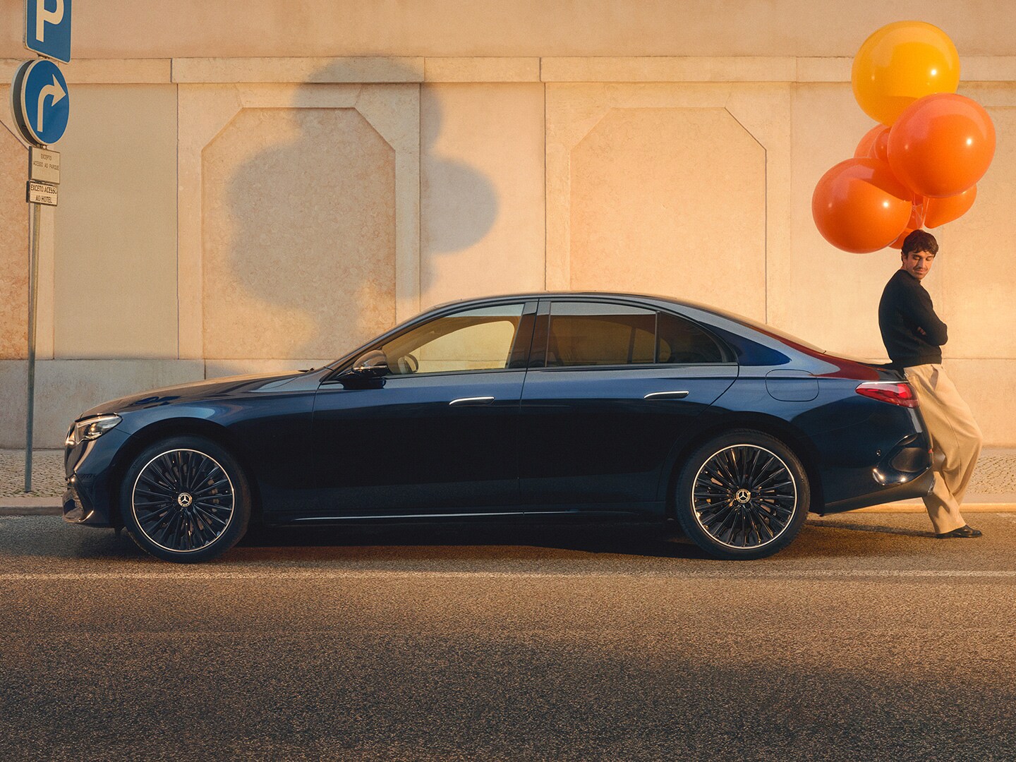 Mann mit orangenen Luftbalons steht an das Heck der Mercedes-Benz E-Klasse angelehnt