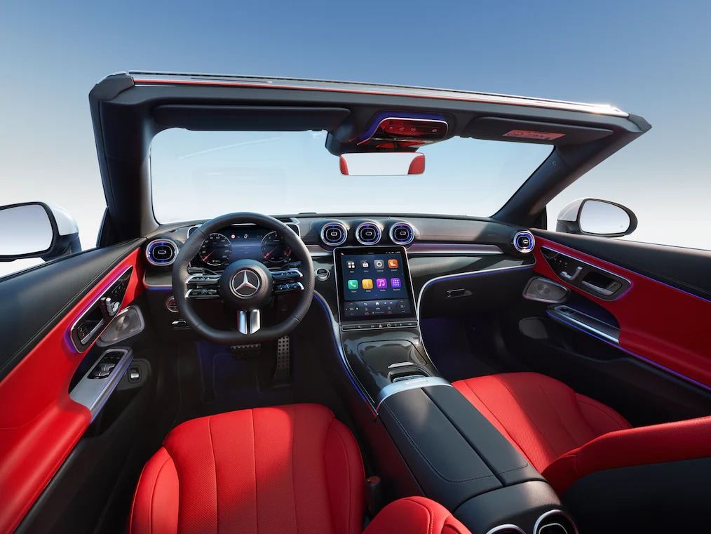 Blick vom Rücksitz auf das Cockpit des Mercedes-Benz CLE Cabriolet mit geöffnetem Verdeck.