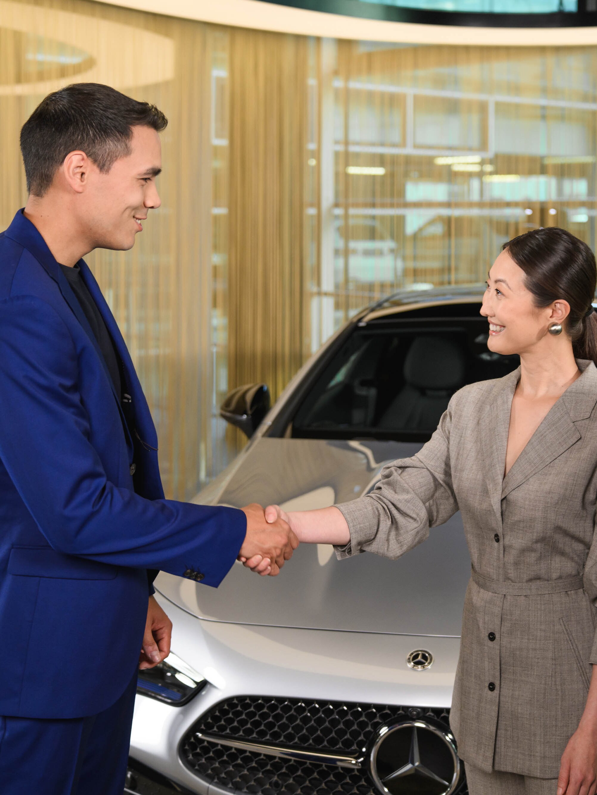 Drei Personen stehen vor einem Mercedes-Benz Fahrzeug und schüteln sich die Hände.