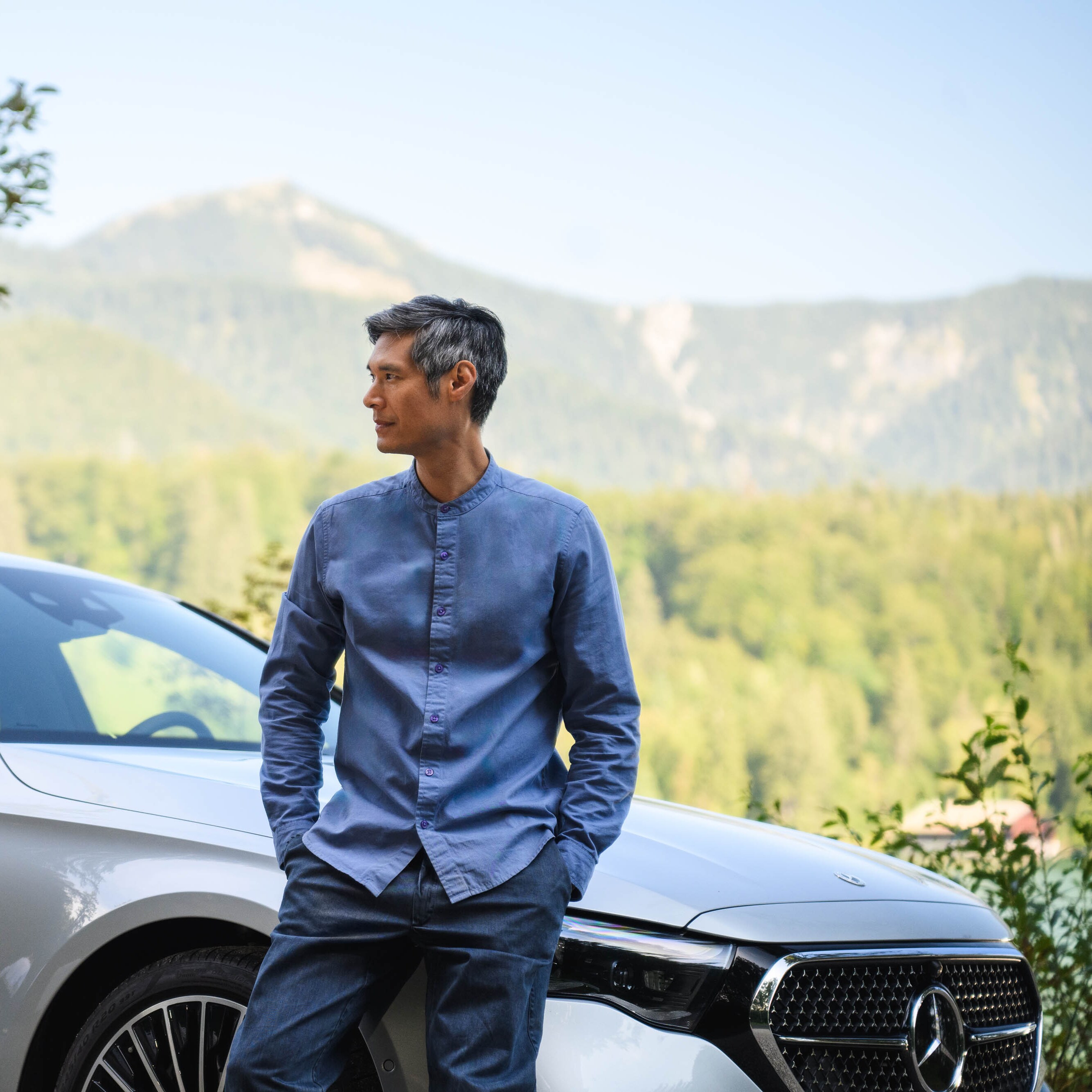 Eine Person steht mit ihrem Mercedes-Benz in der Natur und blickt in die Ferne.
