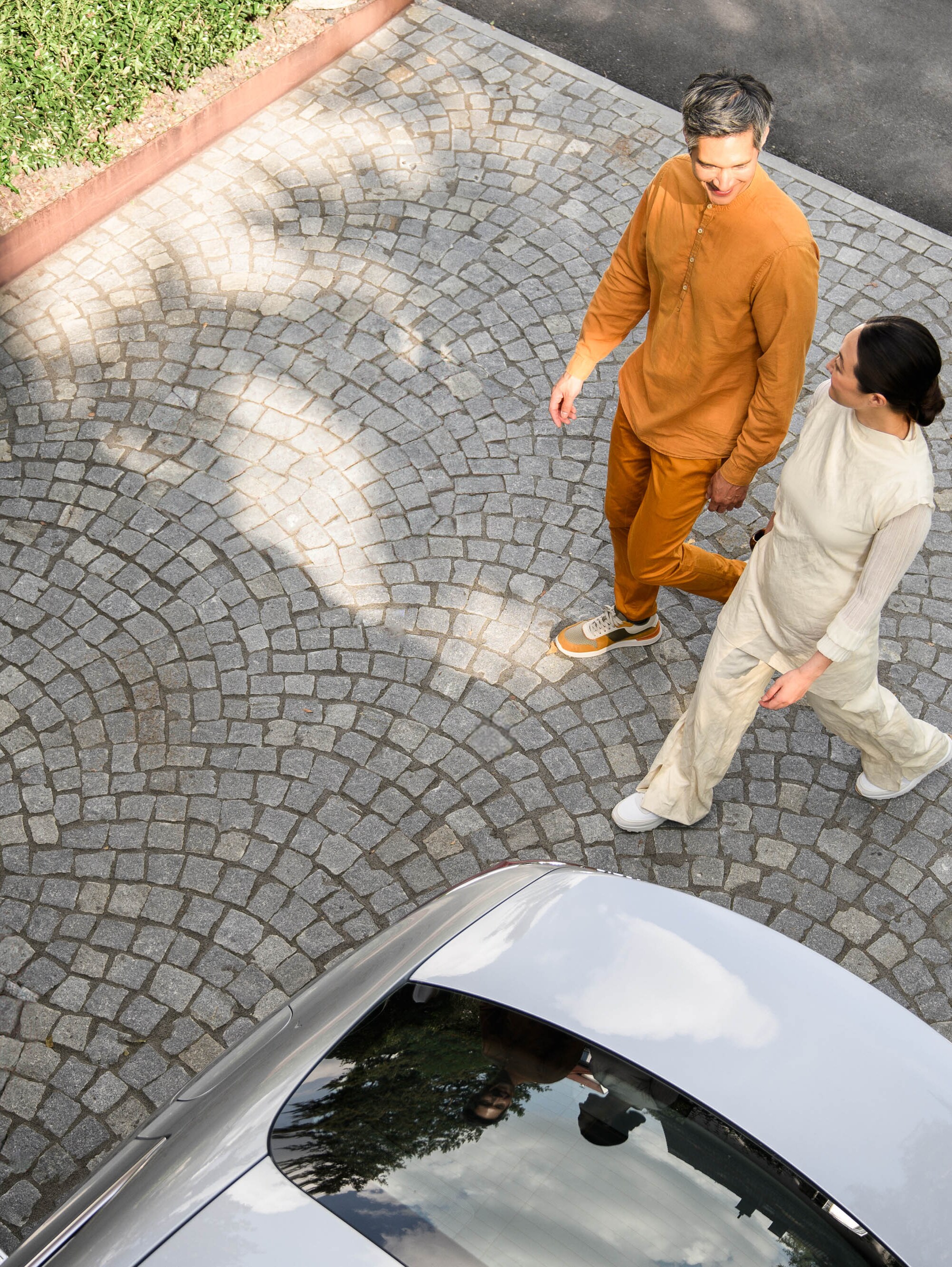 Eine Aufnahme aus hoher Perspektive von zwei Personen, die auf ein Mercedes-Benz Fahrzeug zugehen.
