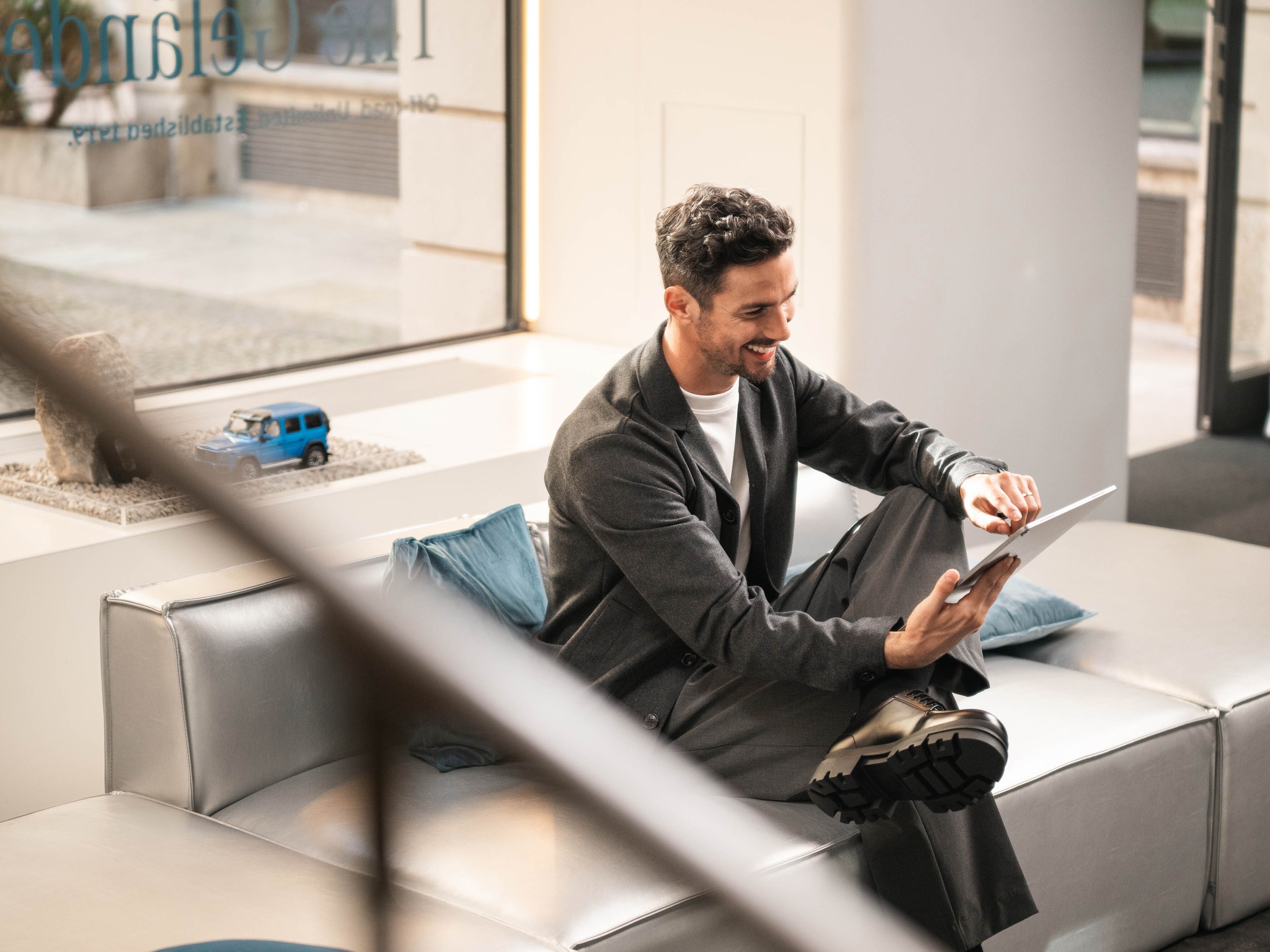 Eine Person auf einem Sofa in einem Schauraum betrachtet ein mobiles Gerät.