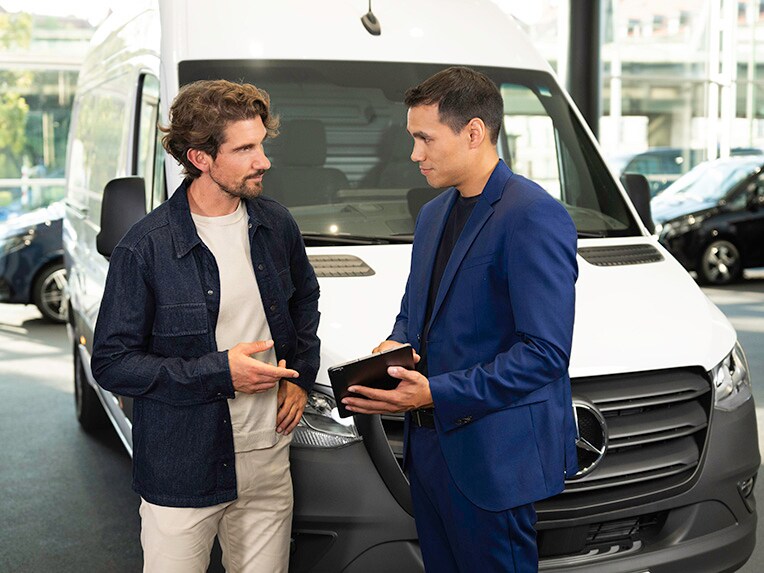 Zwei Personen stehen vor einem Mercedes-Benz Sprinter und schauen auf ein mobiles Gerät.