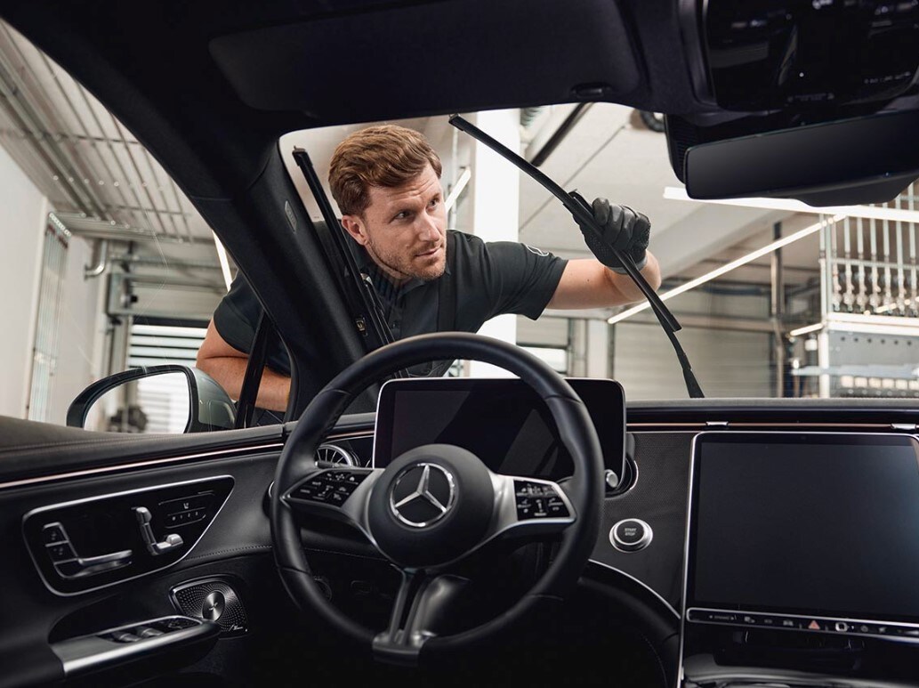 Innenansicht eines Mercedes-Benz-Fahrzeugs, in dem ein Techniker Original-Scheibenwischerblätter austauscht.