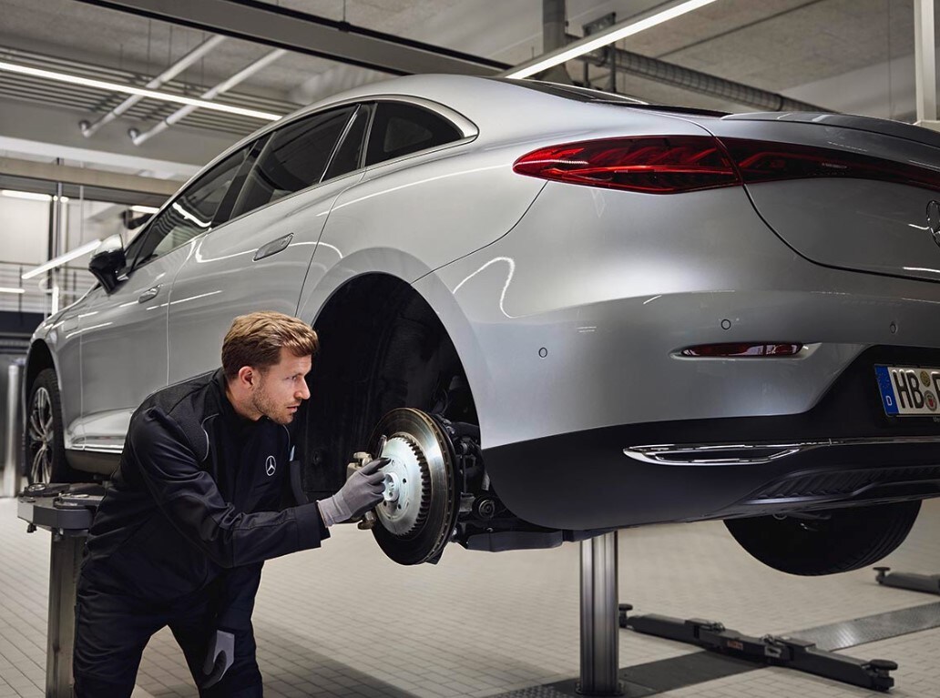 Ein Mercedes-Benz-Fahrzeug steht auf einer Hebebühne, während ein Techniker die hintere Bremsanlage im Rahmen eines Austauschs von Originalteilen überprüft.