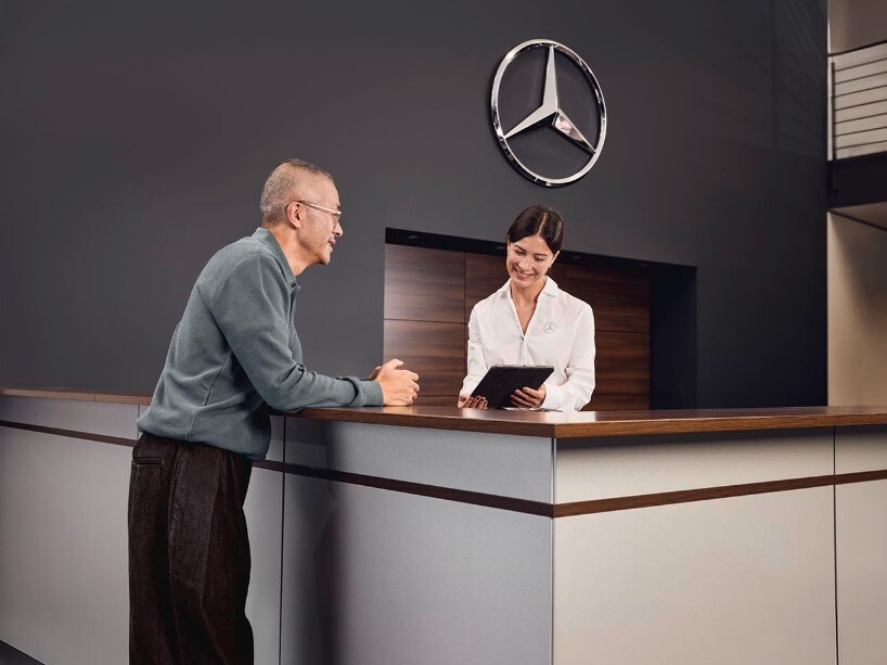 Empfangsbereich der Serviceabteilung eines Mercedes-Benz-Händlers, wo ein Kunde mit einem Serviceberater am Empfang die Einzelheiten der Fahrzeugwartung bespricht.