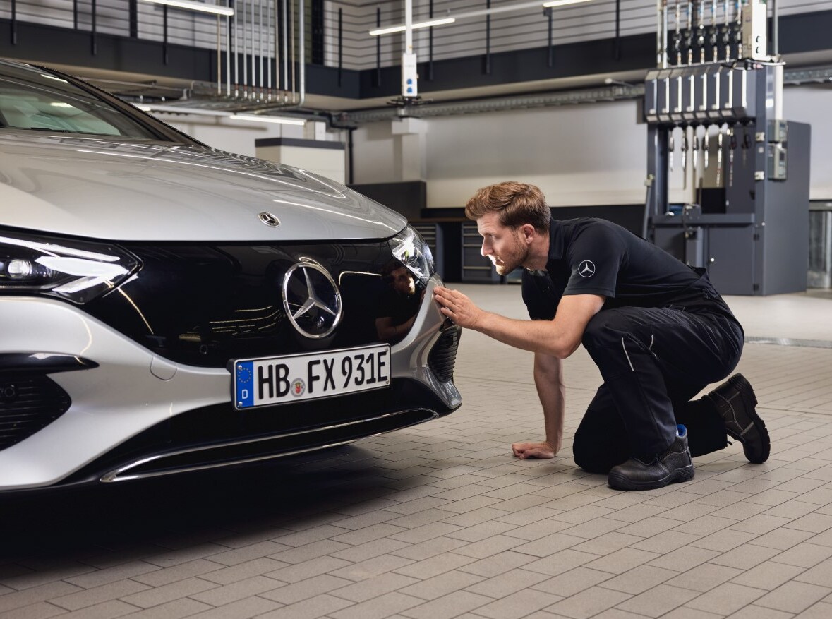Nahaufnahme der Fahrzeugfront eines Mercedes-Benz, an der ein Techniker eine gründliche Prüfung im Zusammenhang mit dem Einbau von Mercedes-Benz Originalteilen durchführt.