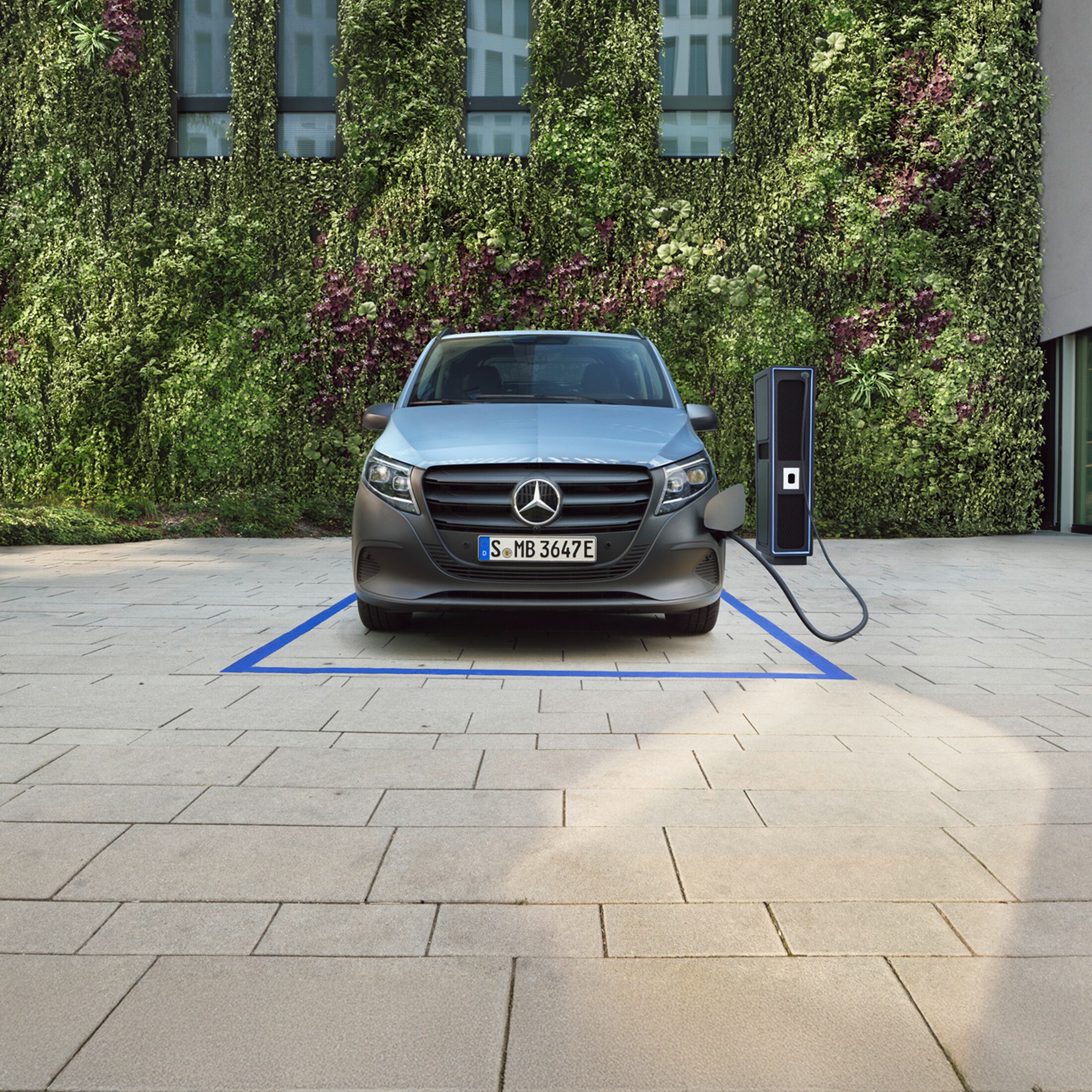 Der Mercedes-Benz eVito auf einem Parkplatz an einer Ladestation vor einer grünen Wand aus Pflanzen