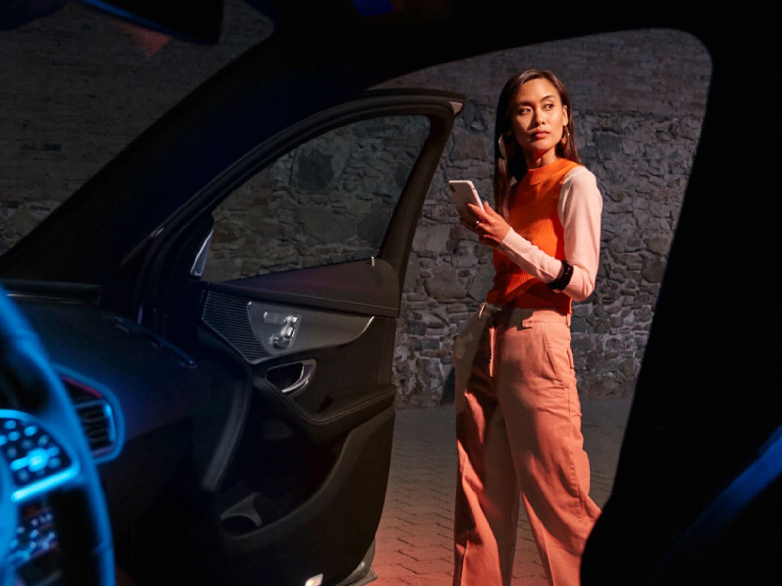 Eine Person steht vor der geöffneten Tür eines Mercedes-Benz EQ Modells und hält ein Smartphone mit geöffneter Mercedes me App in der Hand.
