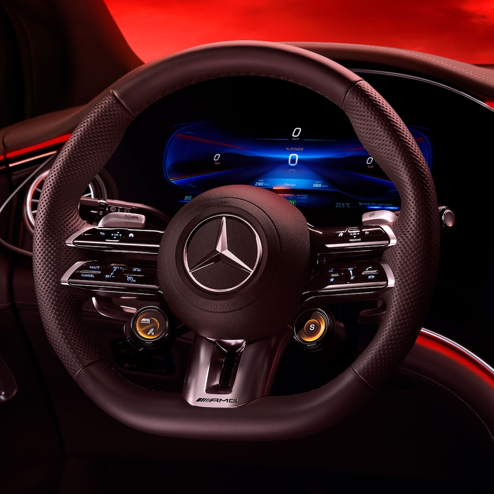 Blick vom Fahrersitz auf das AMG Performance Lenkrad vor einem roten Hintergrund.