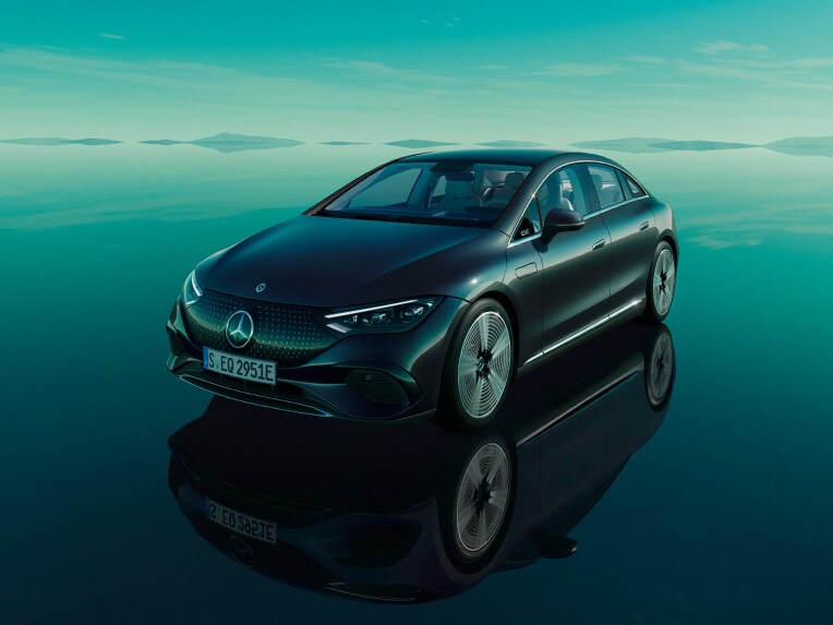 Der vollelektrische EQE von Mercedes-EQ stehend in seiner grünen EQ Welt mit spiegelnder Bodenfläche.