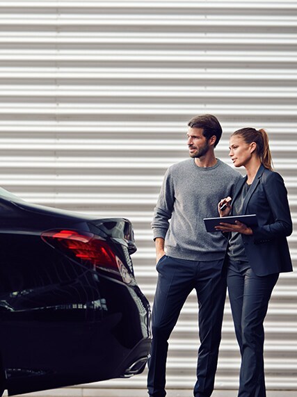 Zwei Personen, die hinter einem Mercedes-Benz Fahrzeug im Verkaufsraum stehen und schauen.