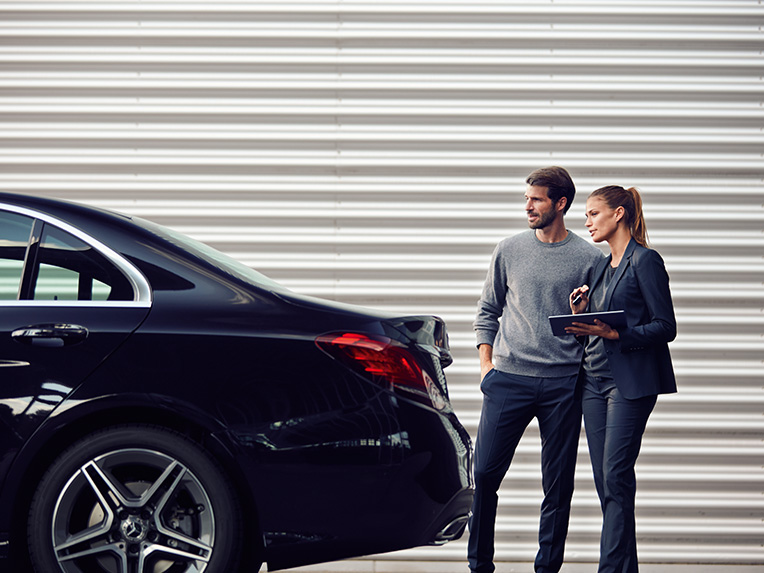 Gebrauchtwagen | Leasing & Finanzierung | Financial Services | Mercedes-Benz Zwei Personen, die hinter einem Mercedes-Benz Fahrzeug im Verkaufsraum stehen und schauen.