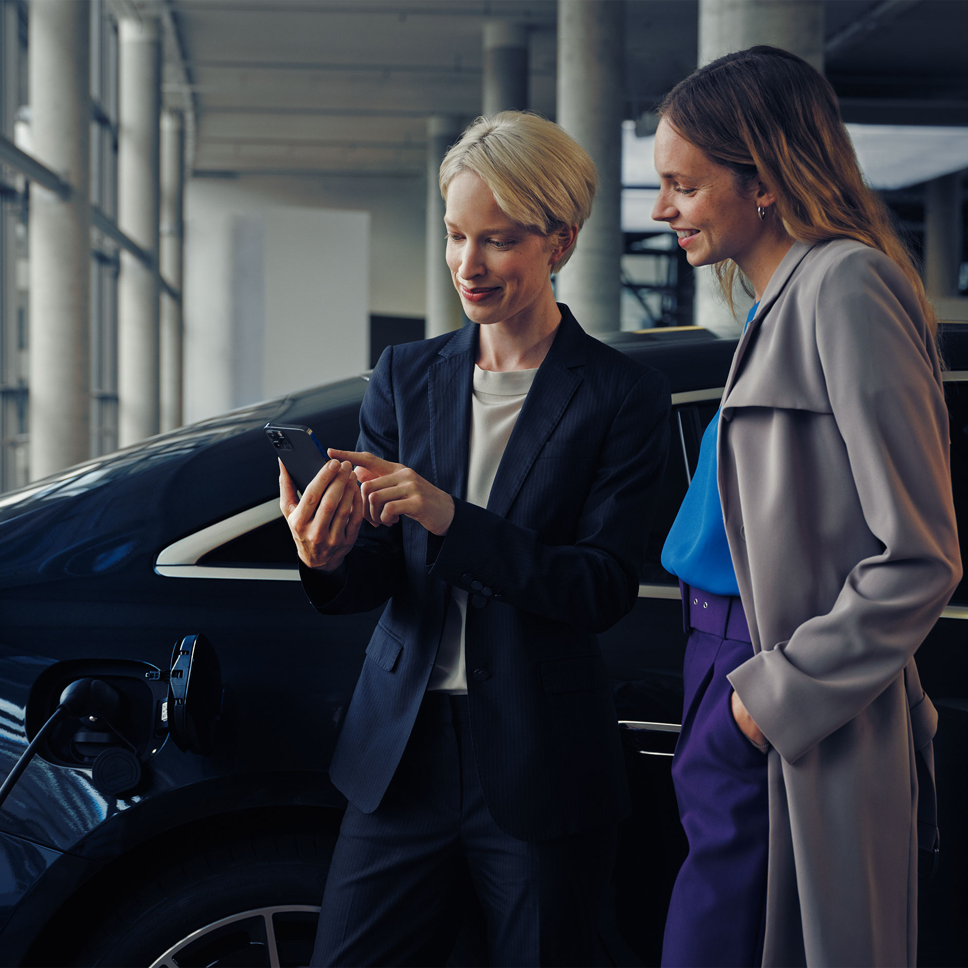 Installationsberatung | Laden | Mercedes-Benz Zwei Frauen vor einer EQE-Limousine, die geladen wird.