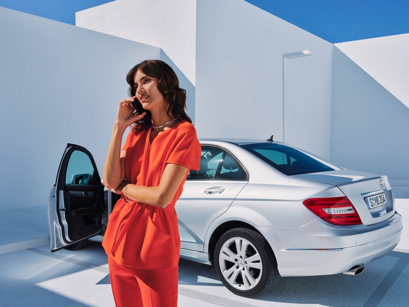 Eine Frau am Telefon vor ihrem Mercedes
