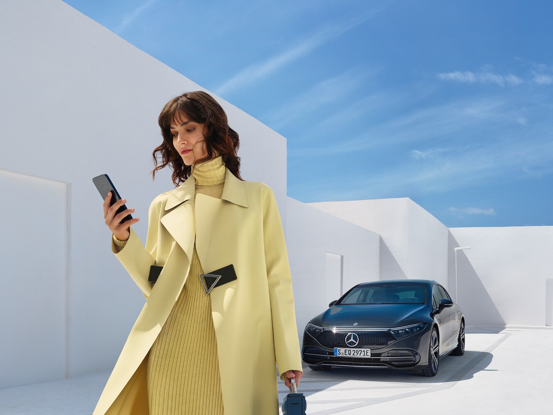 Eine Frau schaut auf ihr Handy während sie von ihrem Mercedes-EQ Fahrzeug weg geht.