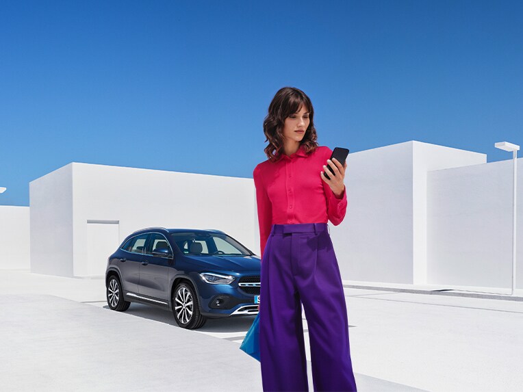 Eine Frau verbindet sich per Smartphone und der Mercedes me App mit ihrem Mercedes Benz und prüft mit den digitalen Extras zum Thema Remote, ob alle Türen ihres Mercedes-Benz verriegelt sind.