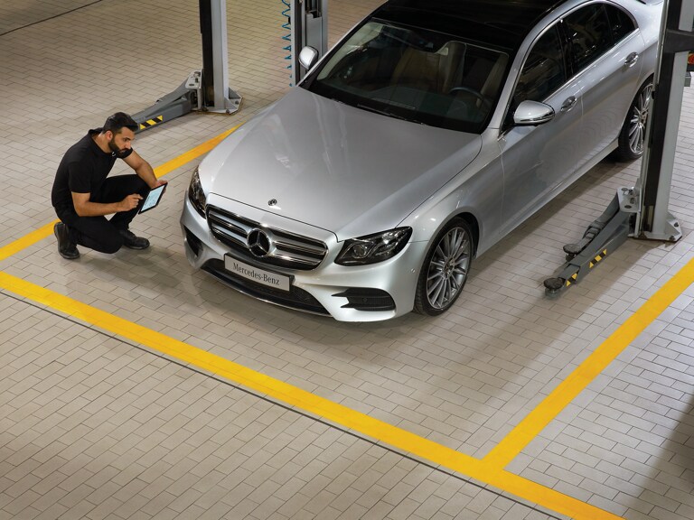 Ein Mercedes-Benz Techniker kniet vor einem Fahrzeug und führt die Hauptuntersuchung durch.