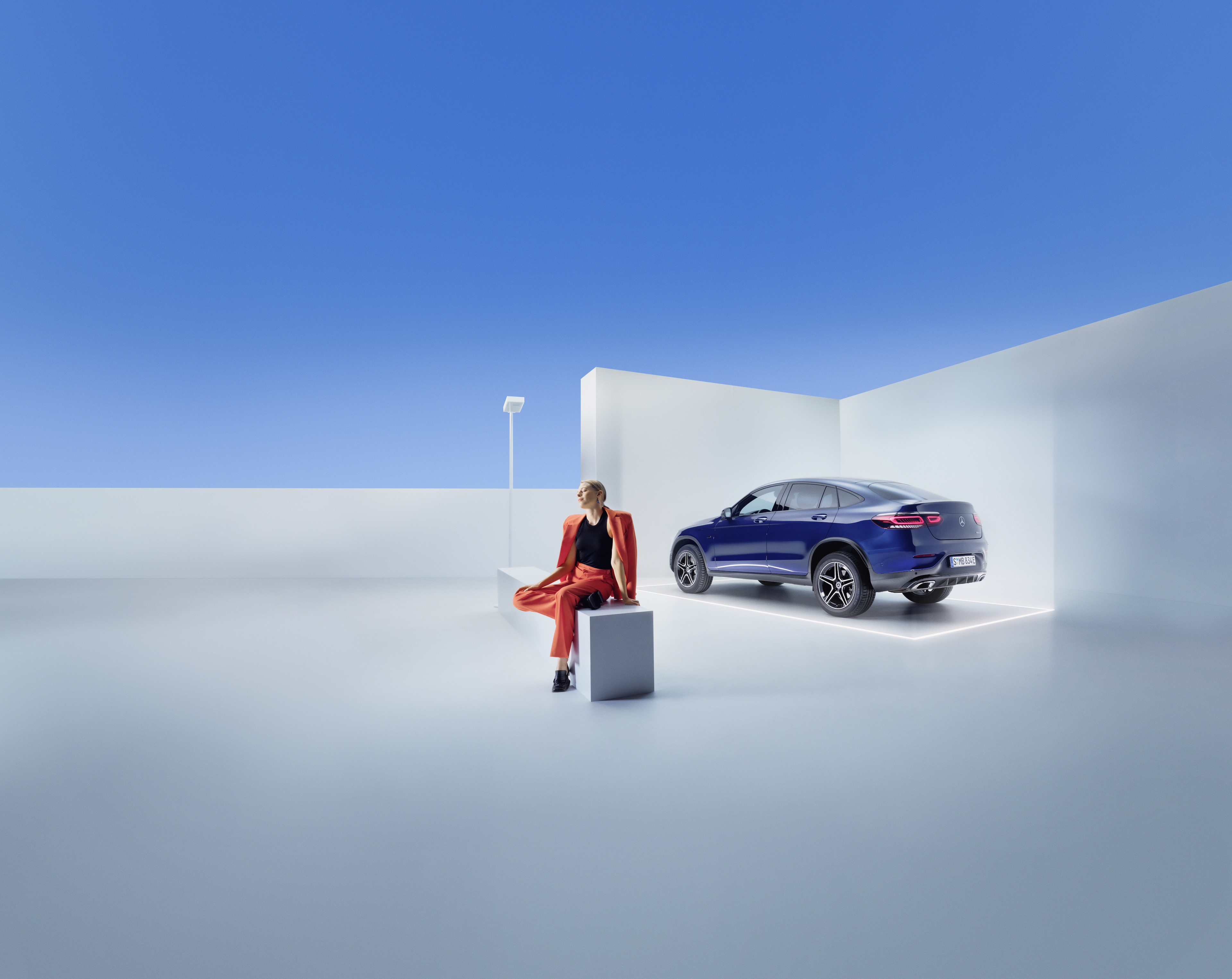 Serviceverträge | Mercedes-Benz Eine Frau sitzt auf einer Bank vor einem Mercedes-Benz.