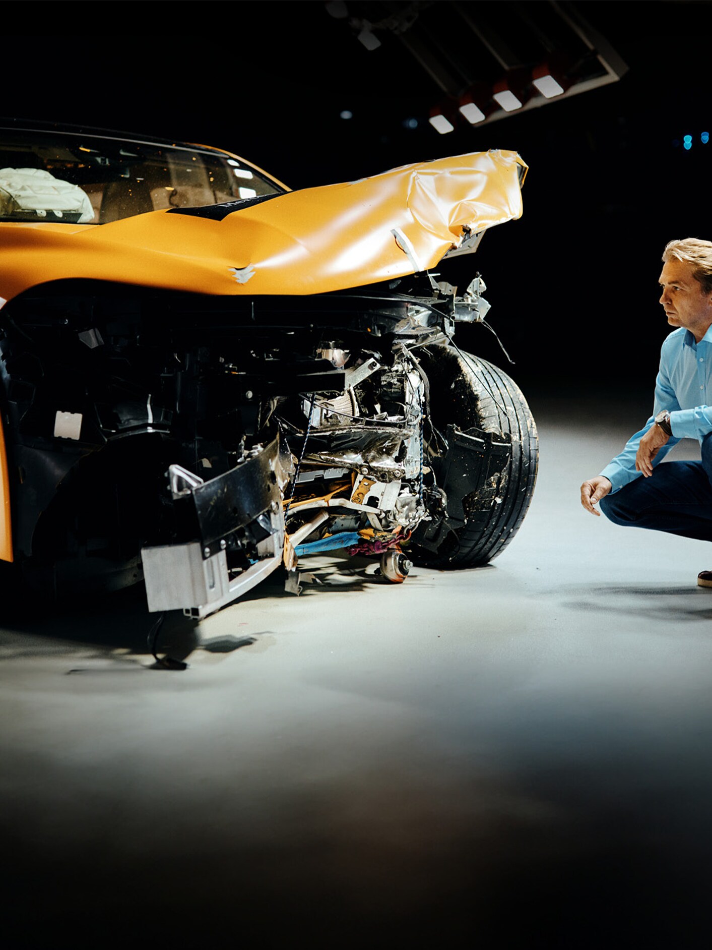 Crashtest-Experte bei der Untersuchung eines frontal beschädigten Mercedes-Benz Fahrzeugs, während er daneben kauert.