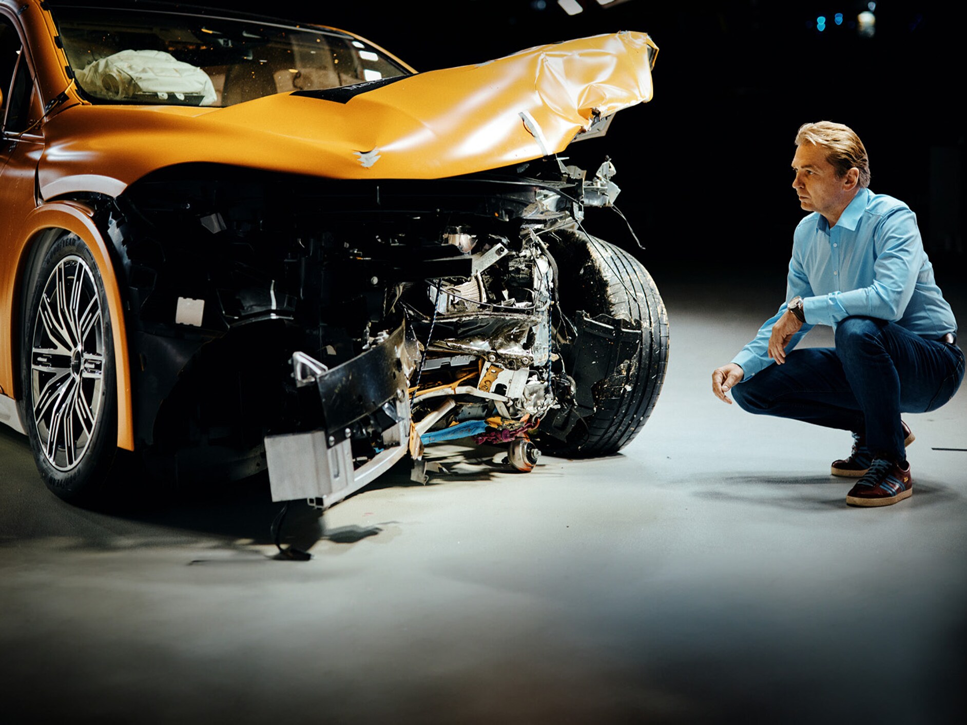 Ein Crashtest-Experte kauert neben einem frontal beschädigten Mercedes-Benz Fahrzeug, das er untersucht.