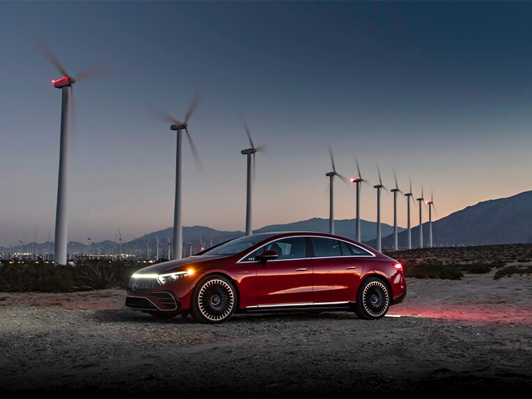 Ein roter Mercedes-Benz EQS (V 297) parkt vor Windkraftanlagen.