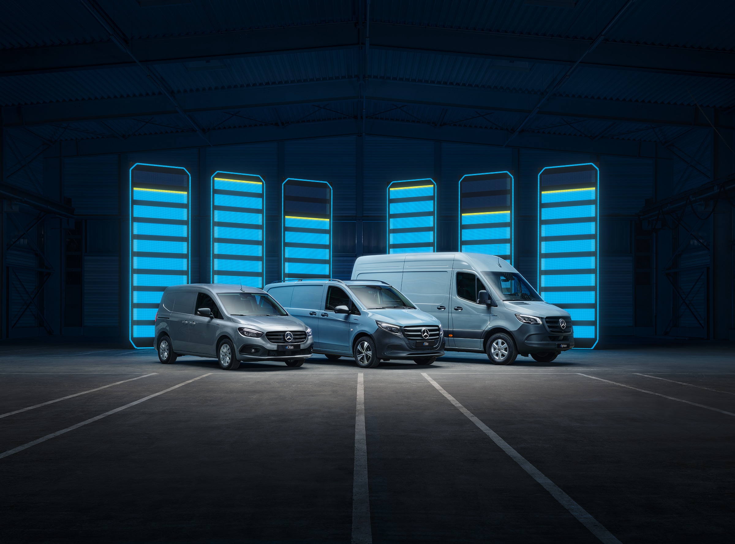 Mercedes-Benz Elektrotransporter-Modellpalette | Geschichte der Nutzfahrzeuge | Mercedes-Benz Die Elektrotransporter-Modellpalette von Mercedes-Benz, ausgestellt in einer futuristischen Lagerhalle mit beleuchteten Ladestationen