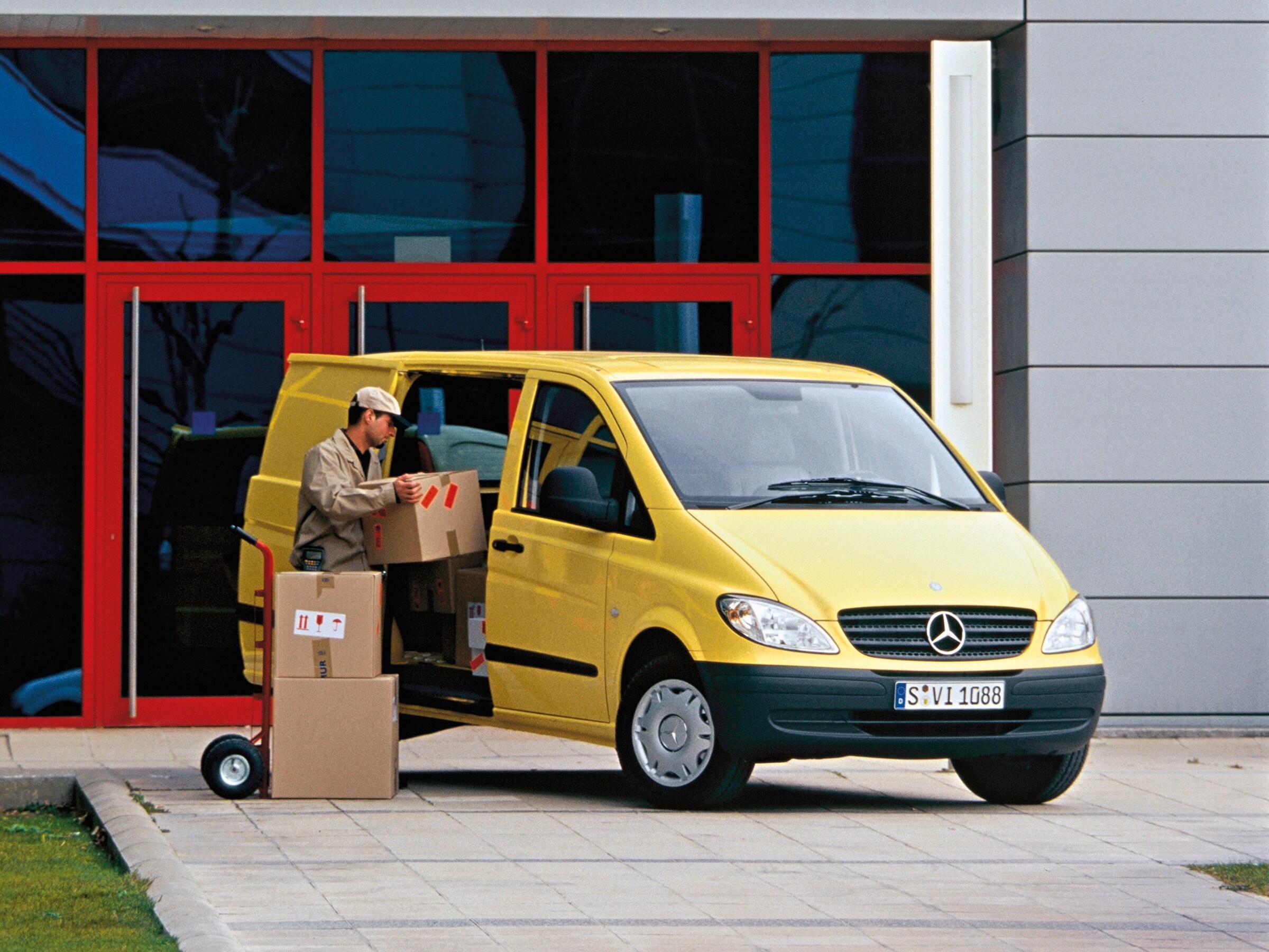 Ein gelber Mercedes-Benz Vito, der vor dem Gebäude geparkt ist, während ein Arbeiter Pakete auslädt