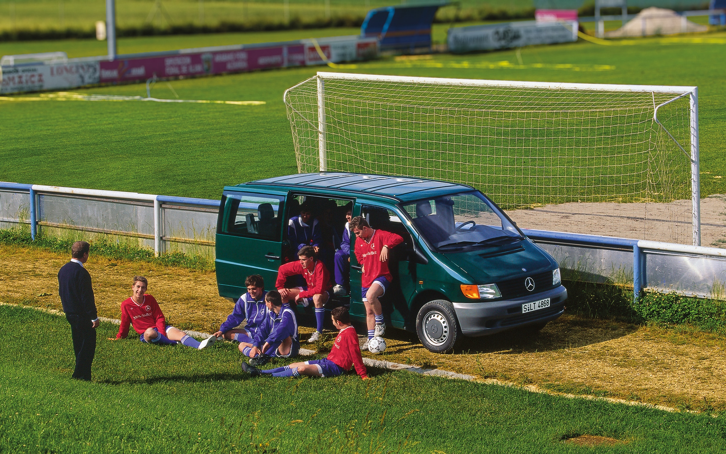 Die erste Generation des Mercedes-Benz Vito | Geschichte der Nutzfahrzeuge | Mercedes-Benz Ein Vito der ersten Generation, der neben einem Fußballplatz geparkt ist, mit Spielern der Mannschaft in der Nähe