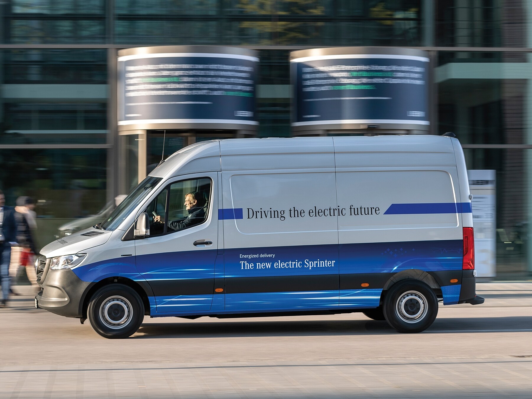 Ein Mercedes-Benz eSprinter Kastenwagen fährt durch eine moderne Stadtstraße