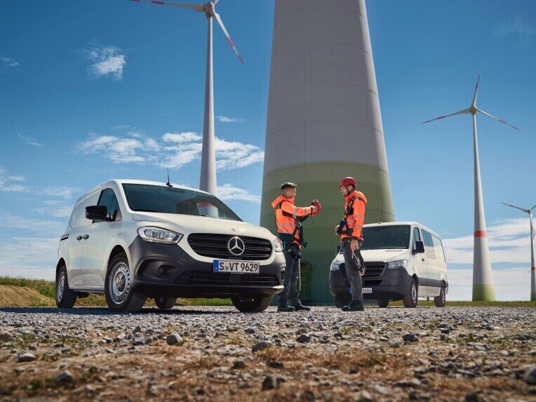 Zwei Transporter von Mercedes-Benz und zwei Personen in Warnkleidung vor einem Windpark.