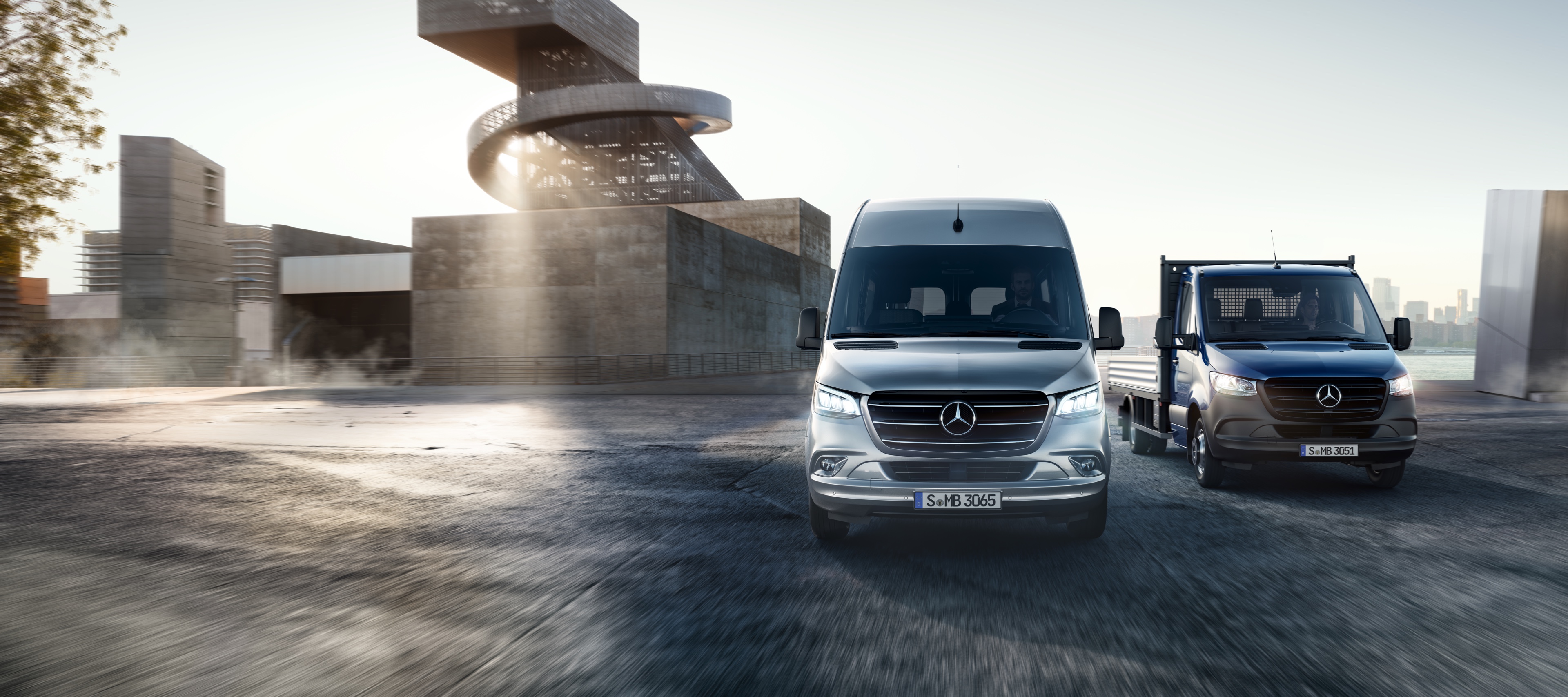 Sprinter | Mercedes-Benz Transporter Der Mercedes-Benz Sprinter als Pritsche und Kastenwagen stehen nebeneinander vor einem modernen Gebäudeensemble.