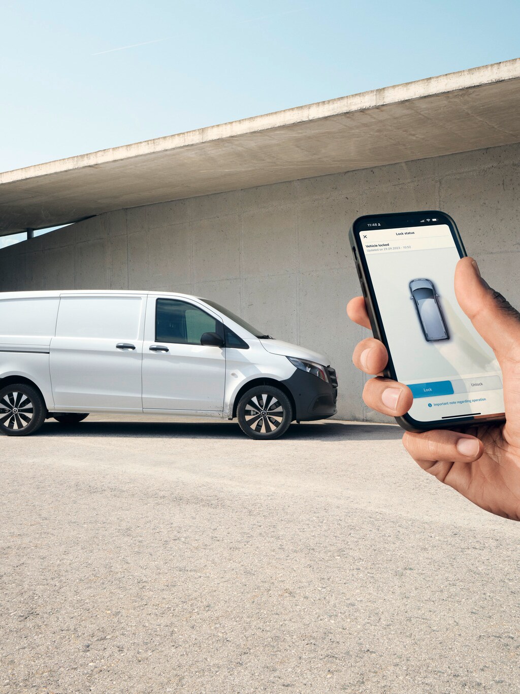 Eine Hand hält ein Smartphone hoch, das die Mercedes-Benz App zeigt. Vito Kastenwagen im Hintergrund.