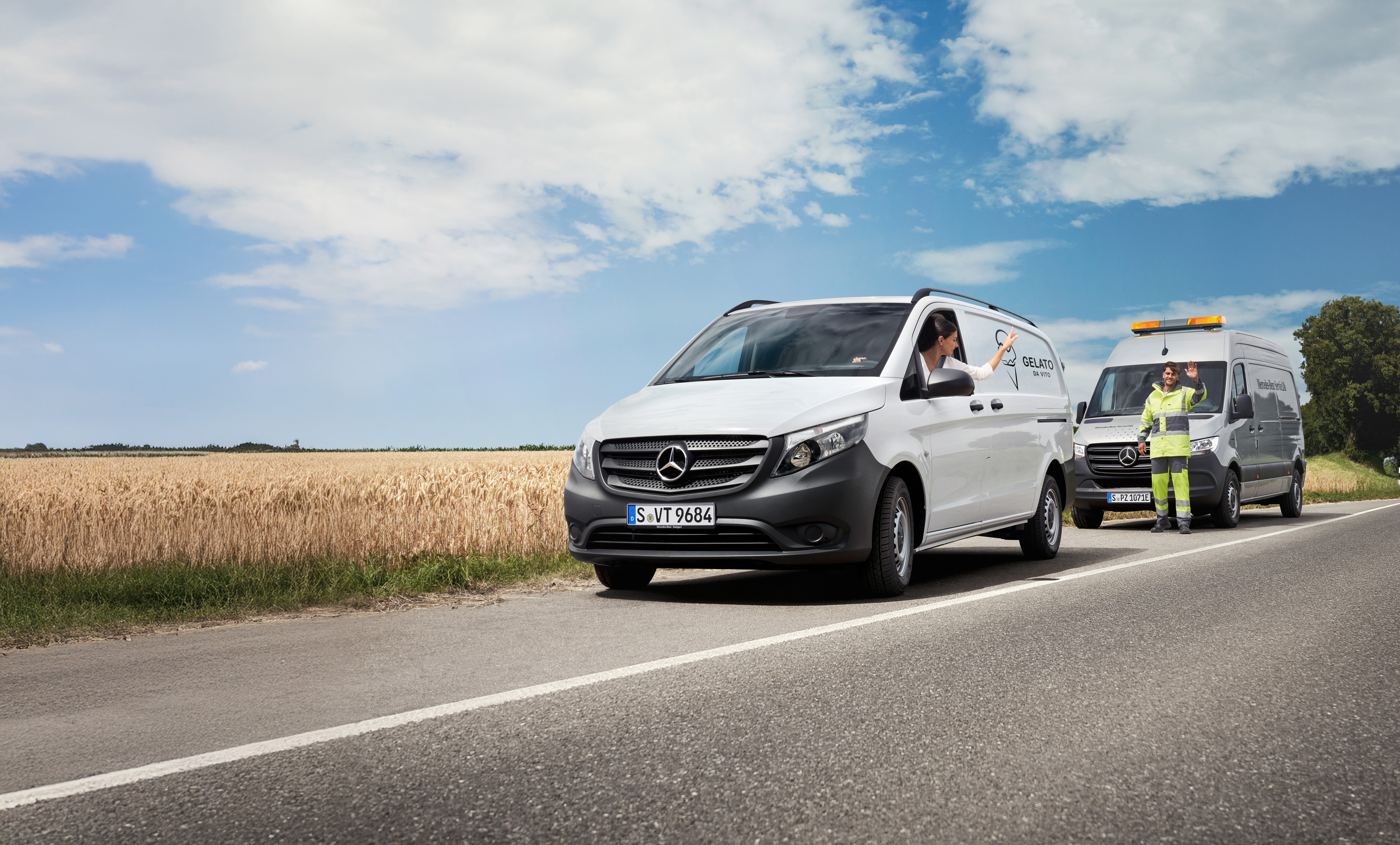 Mercedes-Benz | Transporterbetreuung | Pannenhilfe Eine Person in einem weißen Mercedes-Benz Vito Transporter winkt einem am Straßenrand geparkten Servicetechniker zu.