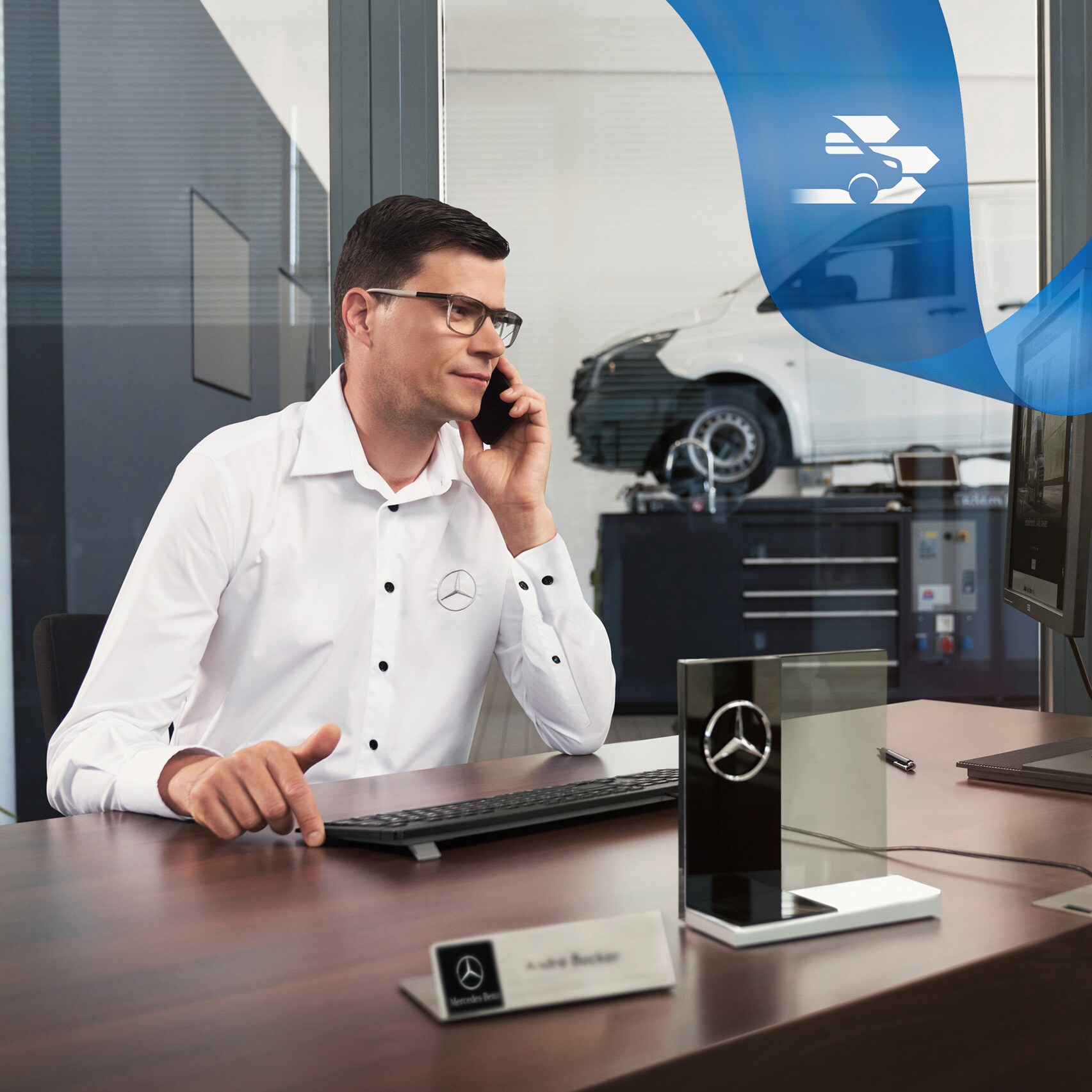 Ein Angestellter am Schreibtisch telefoniert, im Hintergrund ein Mercedes-Benz Vito in der Werkstatt.