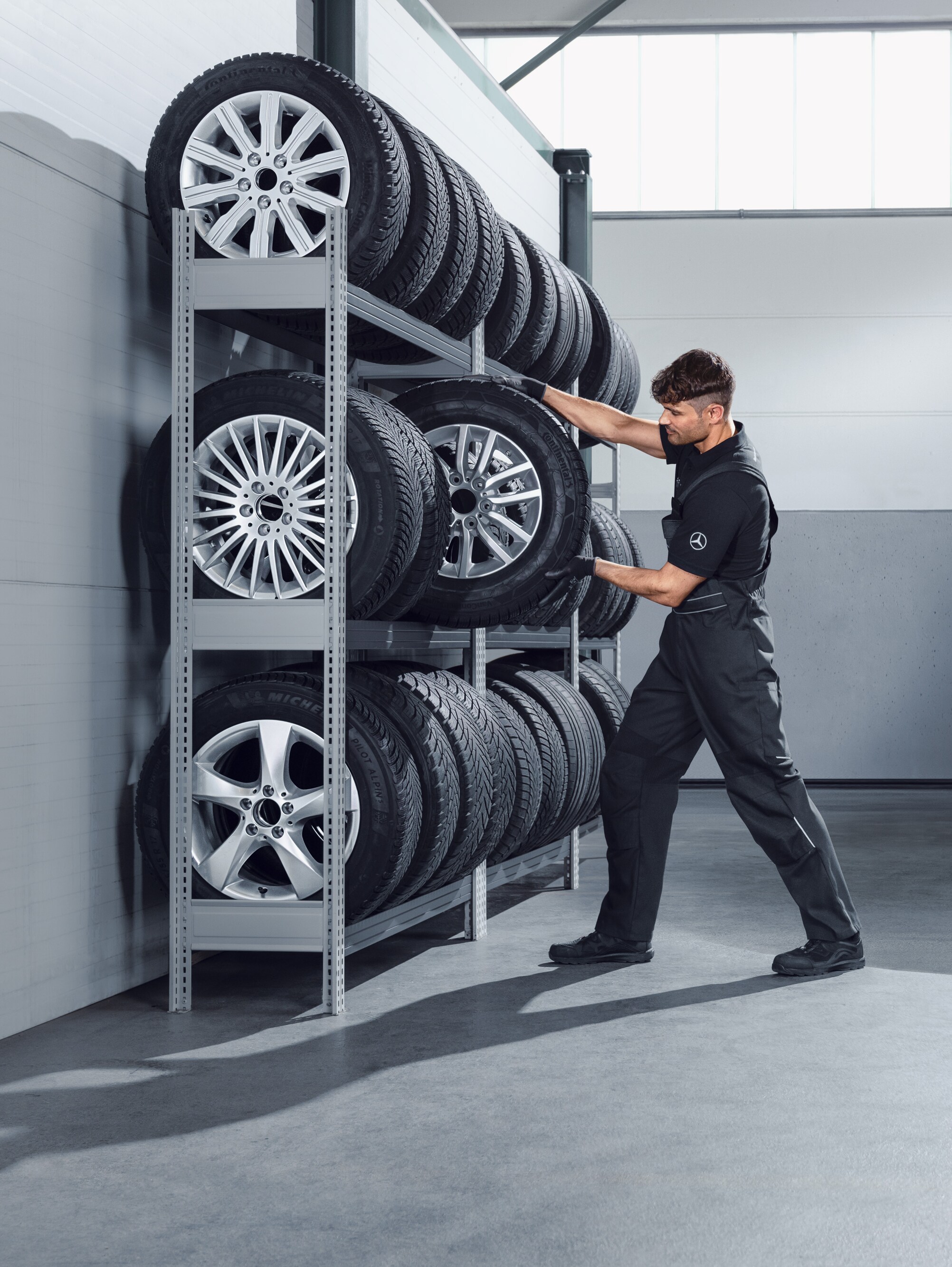 Mechaniker sucht Mercedes-Benz Winterkompletträder für einen weißen Sprinter aus dem Werkstattregal aus.