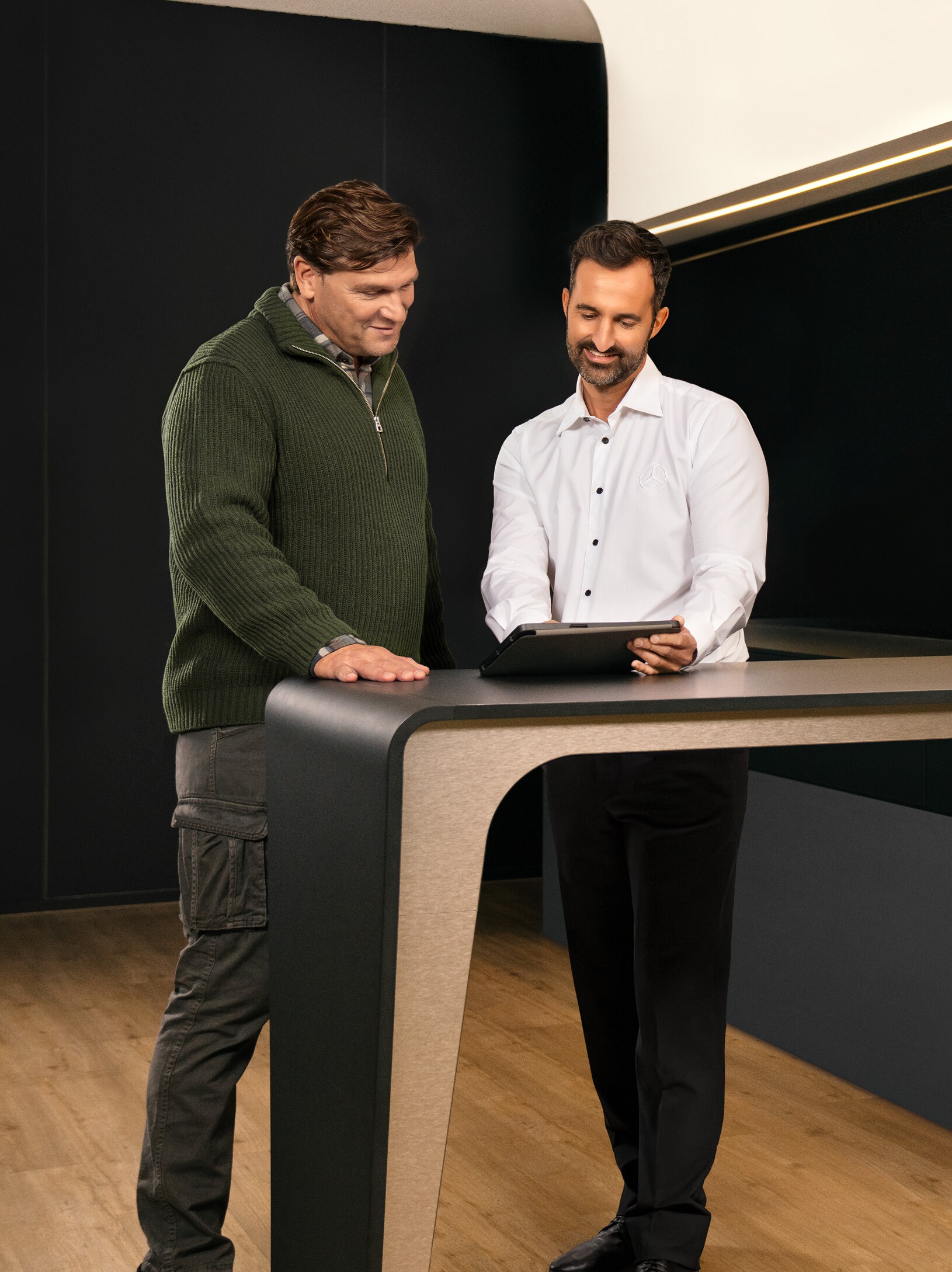 Zwei Männer in einem Beratungsgespräch stehen um einen Tisch herum und schauen auf ein iPad.