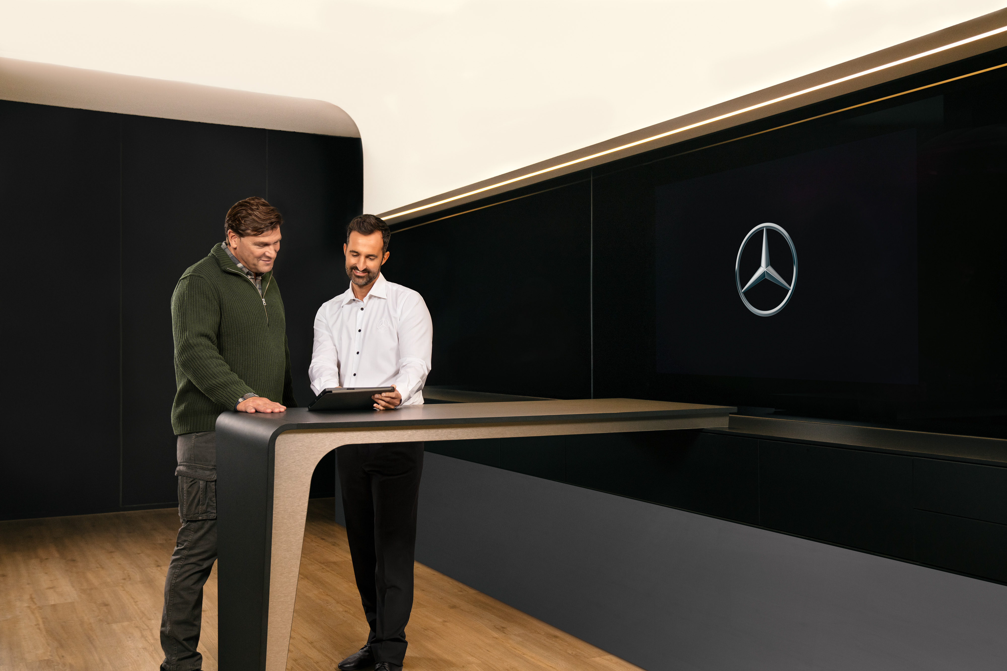 Mercedes-Benz | ServiceCare Transporter Zwei Männer in einem Beratungsgespräch stehen um einen Tisch herum und schauen auf ein iPad.