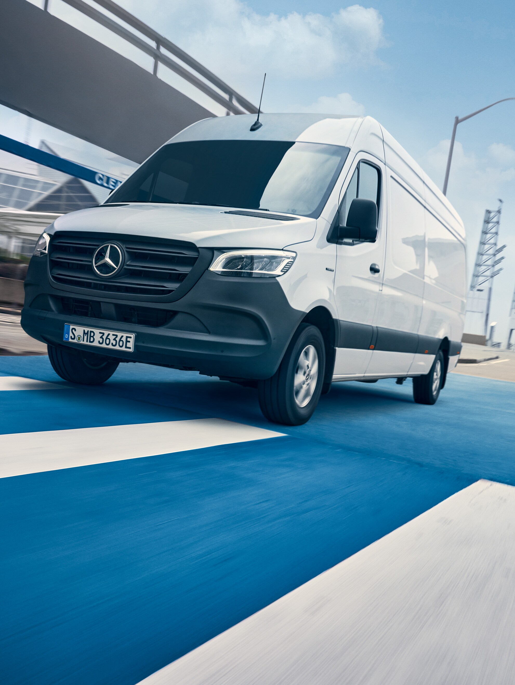 Ein weißer Mercedes-Benz Sprinter fährt auf einer Straße durch eine Stadt.