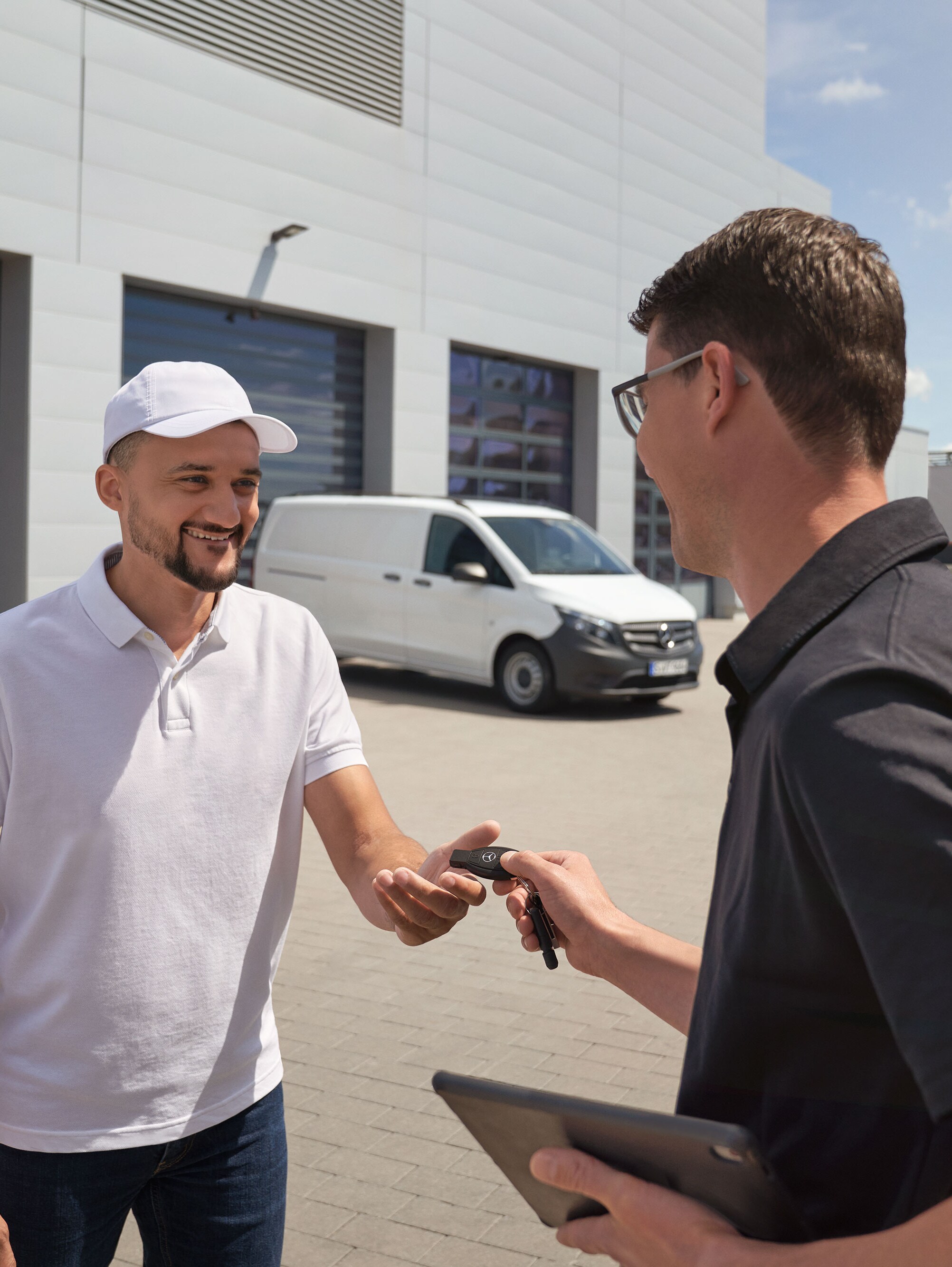 Ein Techniker bei der Übergabe eines Schlüsselanhängers an einen Kunden, im Hintergrund ein weißer Mercedes-Benz Vito.