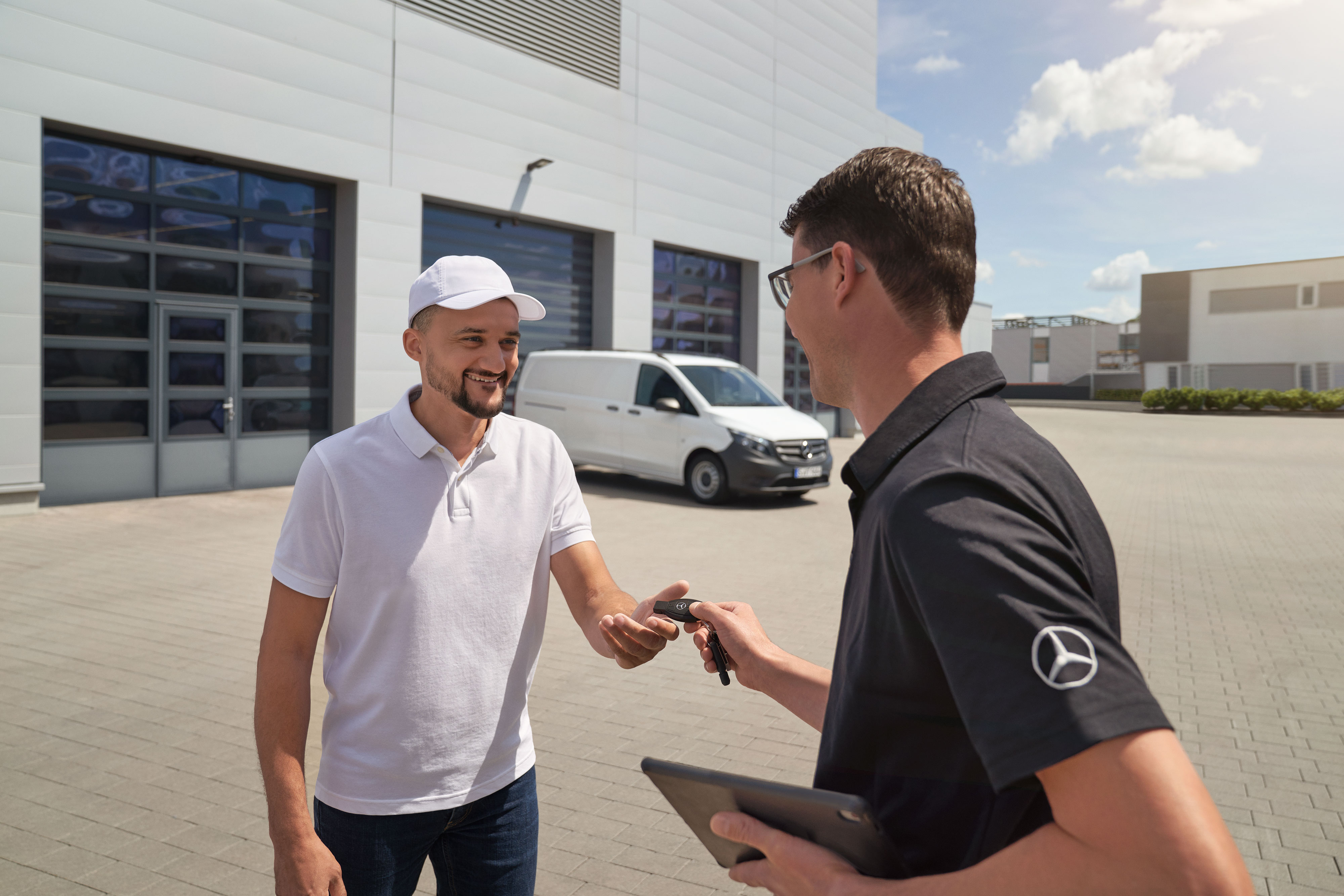 Mercedes-Benz | ServiceCare Transporter | Zusatzoptionen Ein Techniker bei der Übergabe eines Schlüsselanhängers an einen Kunden, im Hintergrund ein weißer Mercedes-Benz Vito.
