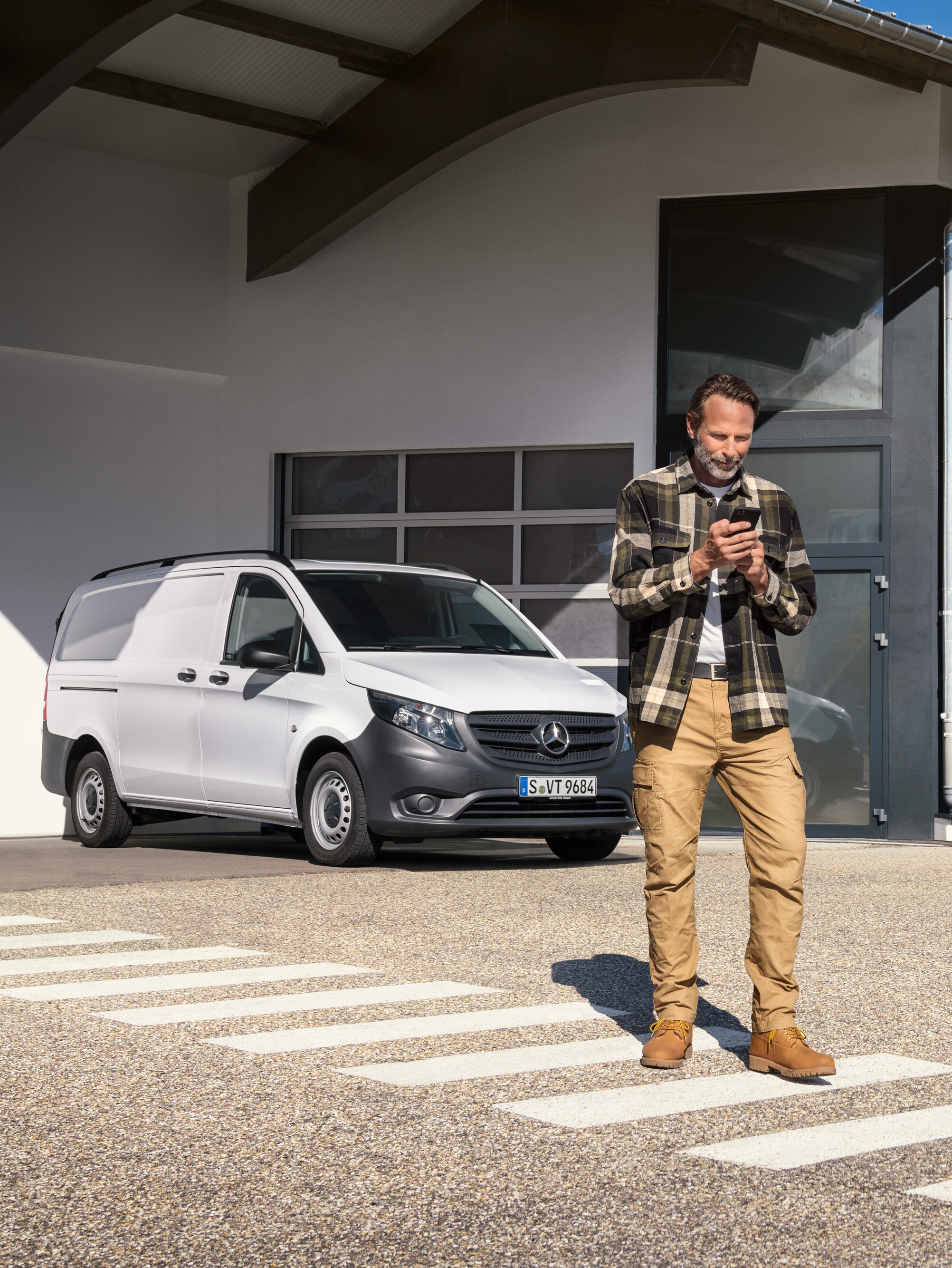 Ein Mann steht vor einem weißen Mercedes-Benz Vito und benutzt sein Smartphone.