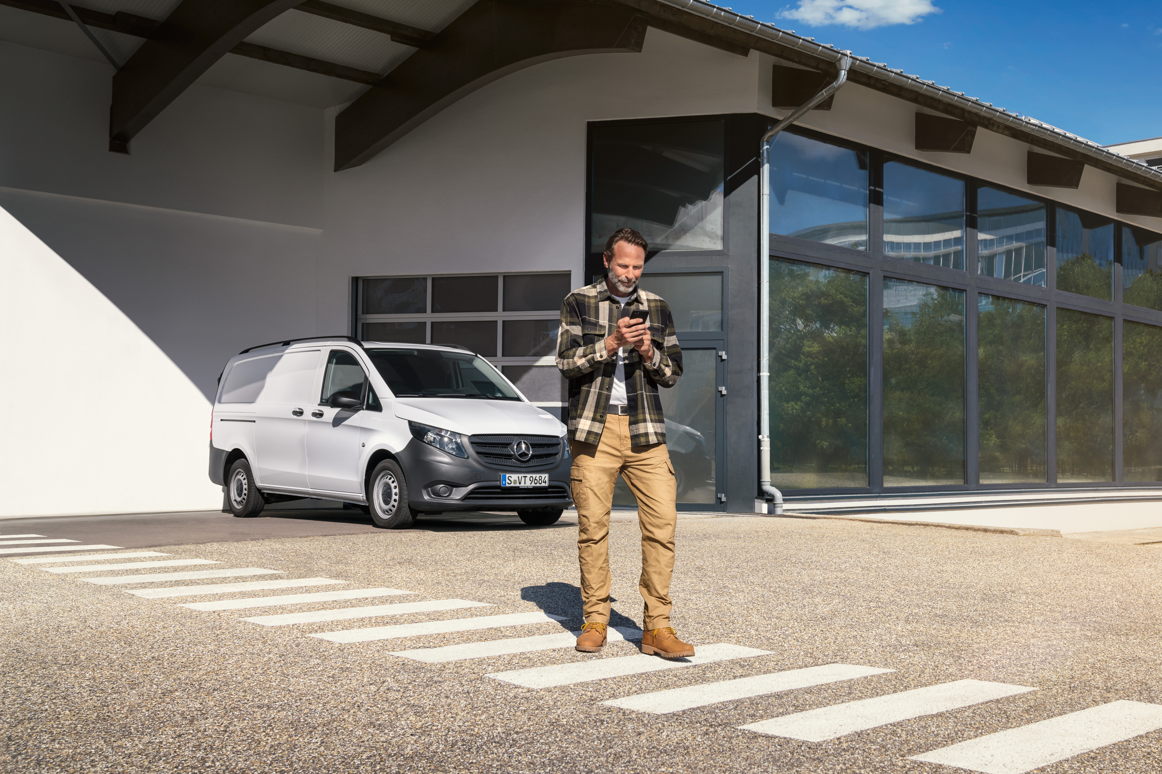 Mercedes-Benz | Elektrofahrzeug-Service | Digitale Unterstützung Ein Mann steht vor einem weißen Mercedes-Benz Vito und benutzt sein Smartphone.