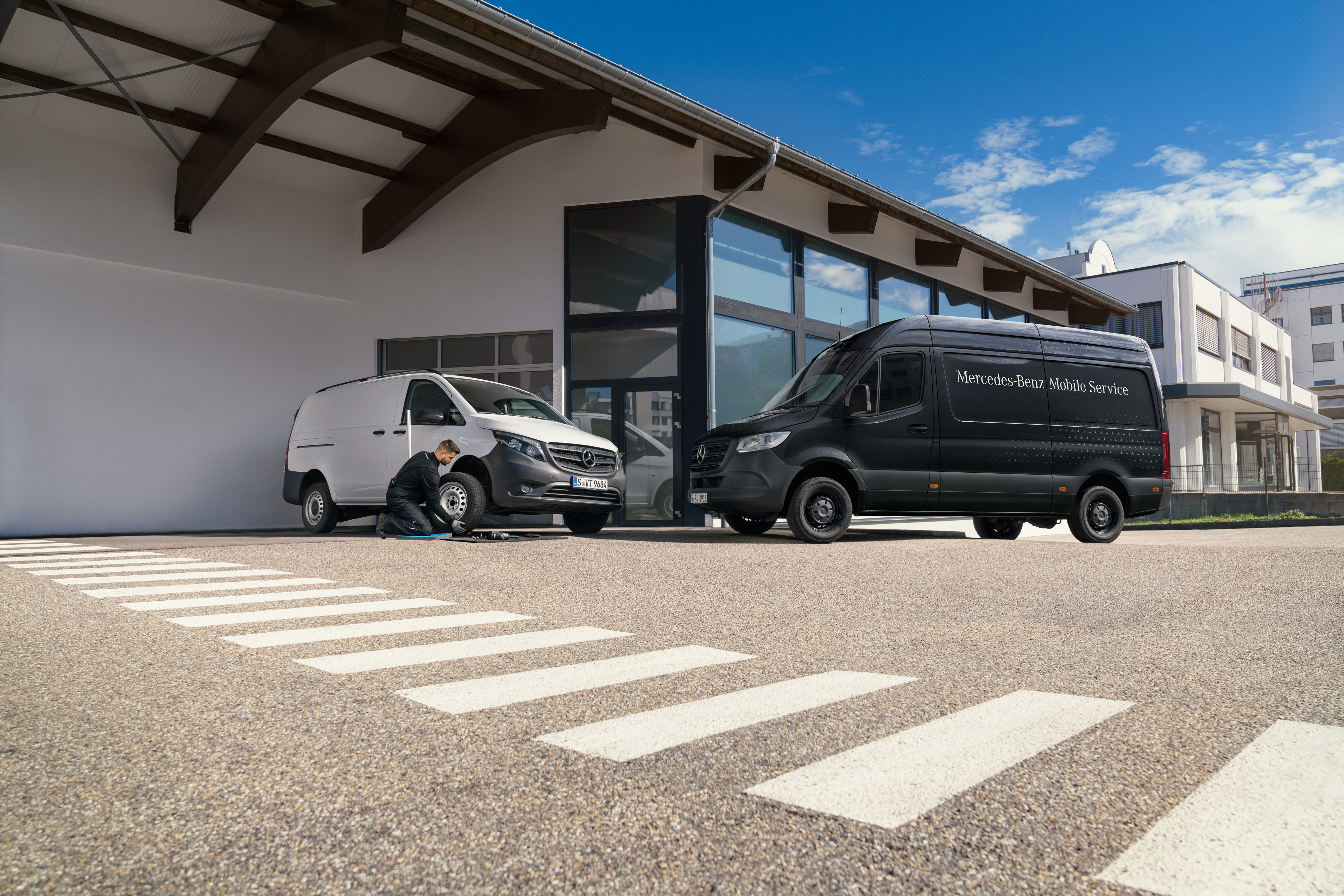Mercedes-Benz | Mobiler Service | Bremsanlage Ein Techniker wechselt einen Reifen an einem weißen Mercedes-Benz Vito vor einem Ausstellungsraum.