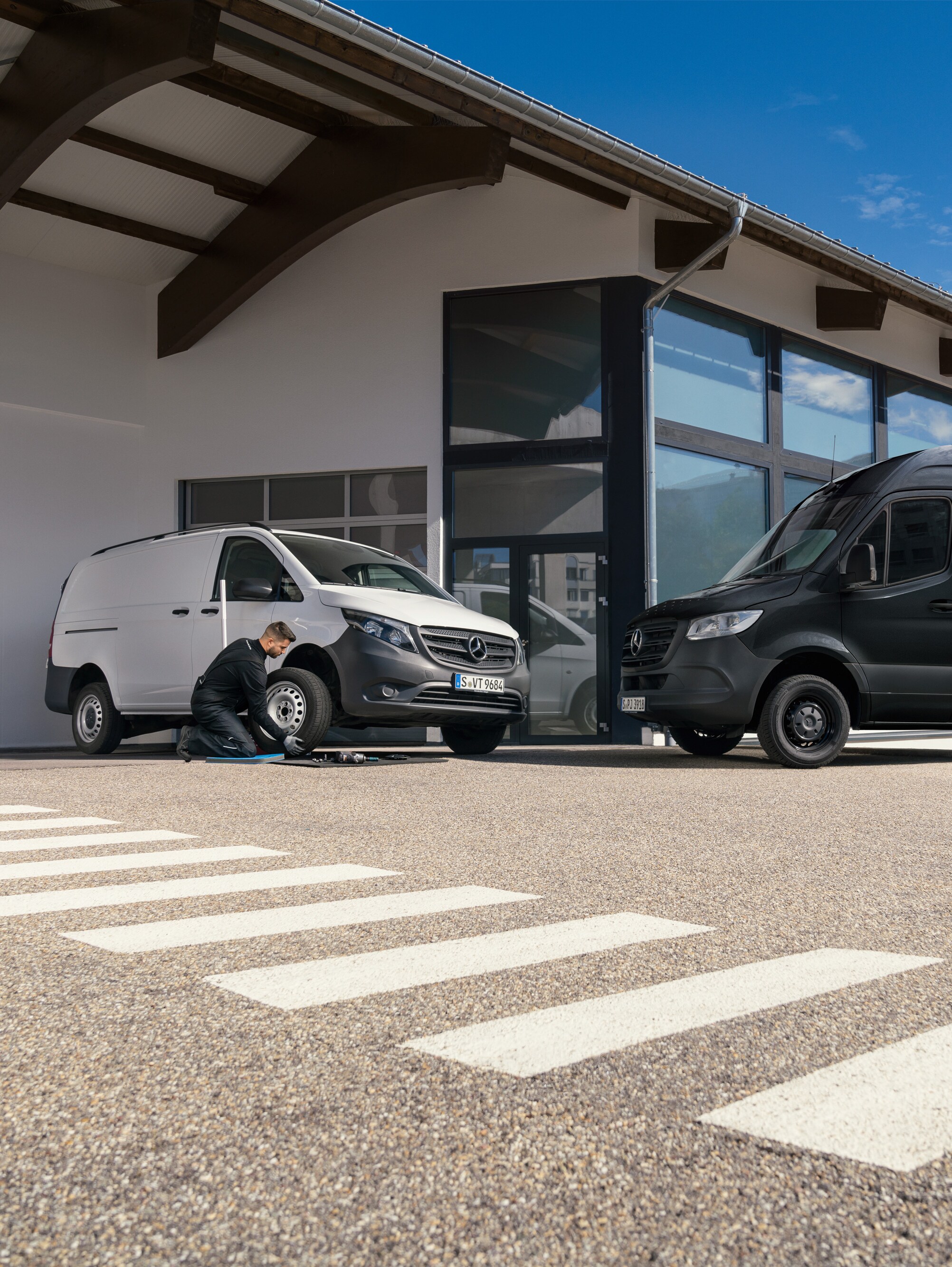 Ein Techniker wechselt einen Reifen an einem weißen Mercedes-Benz Vito vor einem Ausstellungsraum.