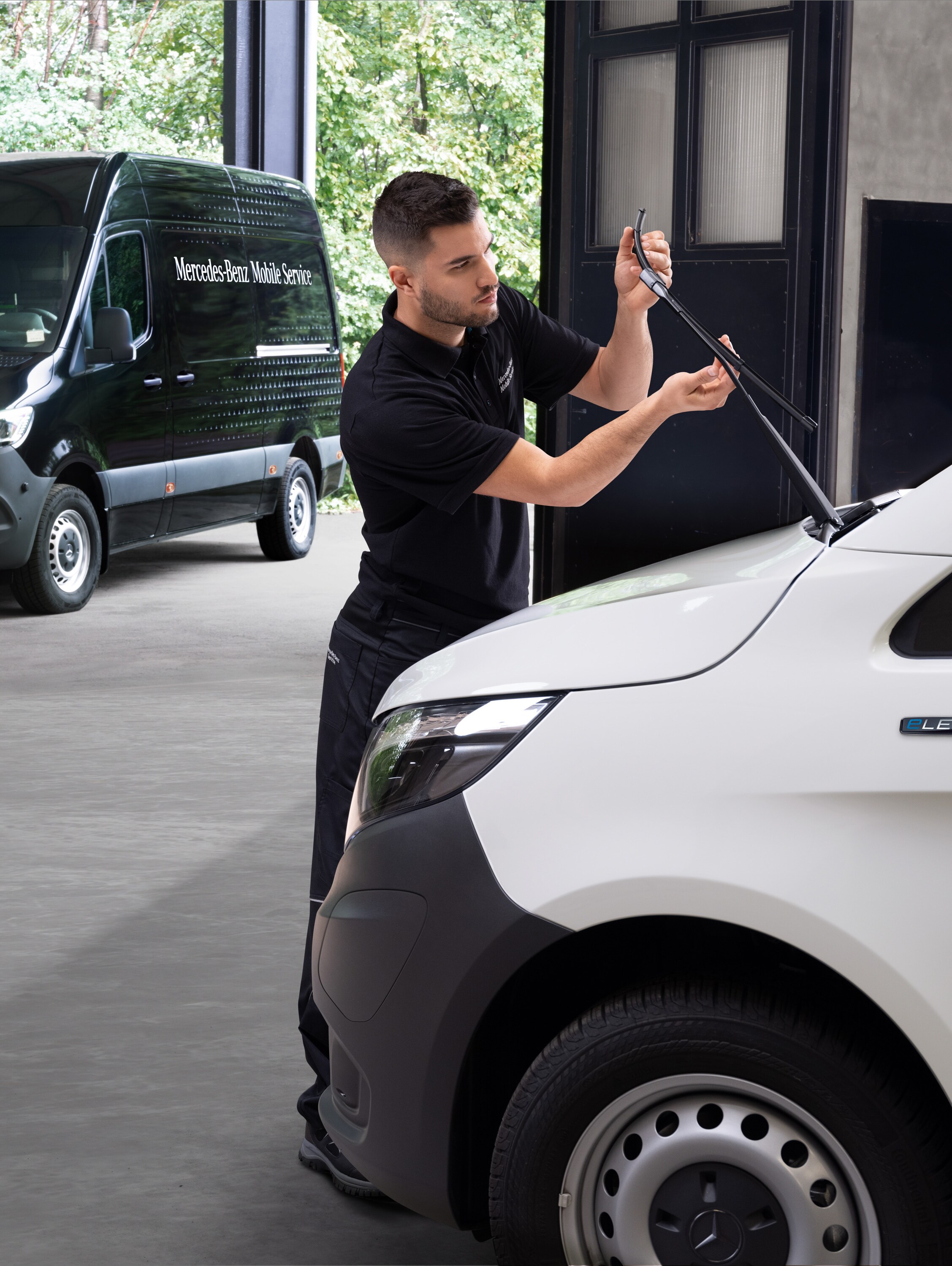 Ein Techniker wechselt die Wischerblätter an einem weißen Mercedes-Benz Vito Transporter.