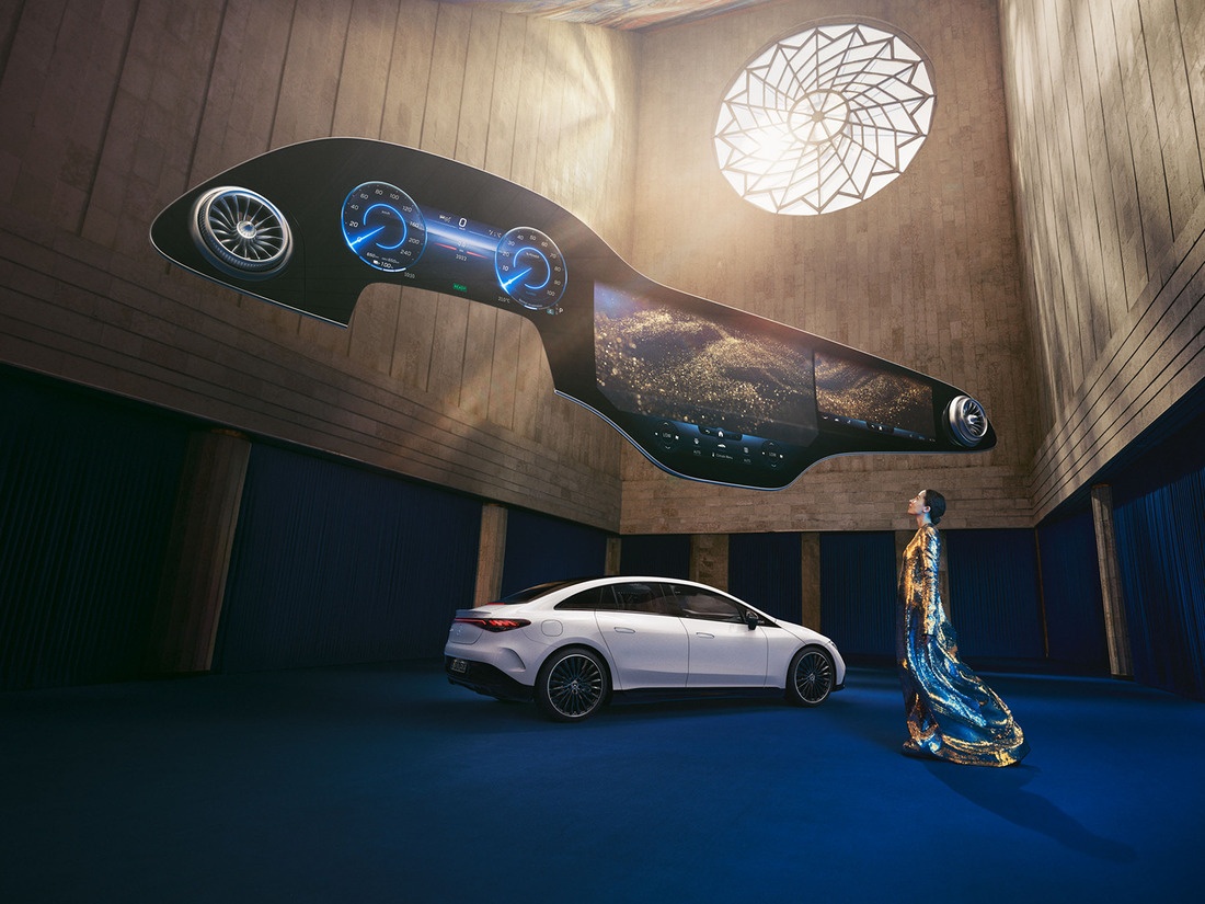 Mercedes-Benz Hyperscreen Eine Frau steht vor dem Mercedes-Benz EQ Fahrzeug mit über ihr schwebendem Hyperscreen.